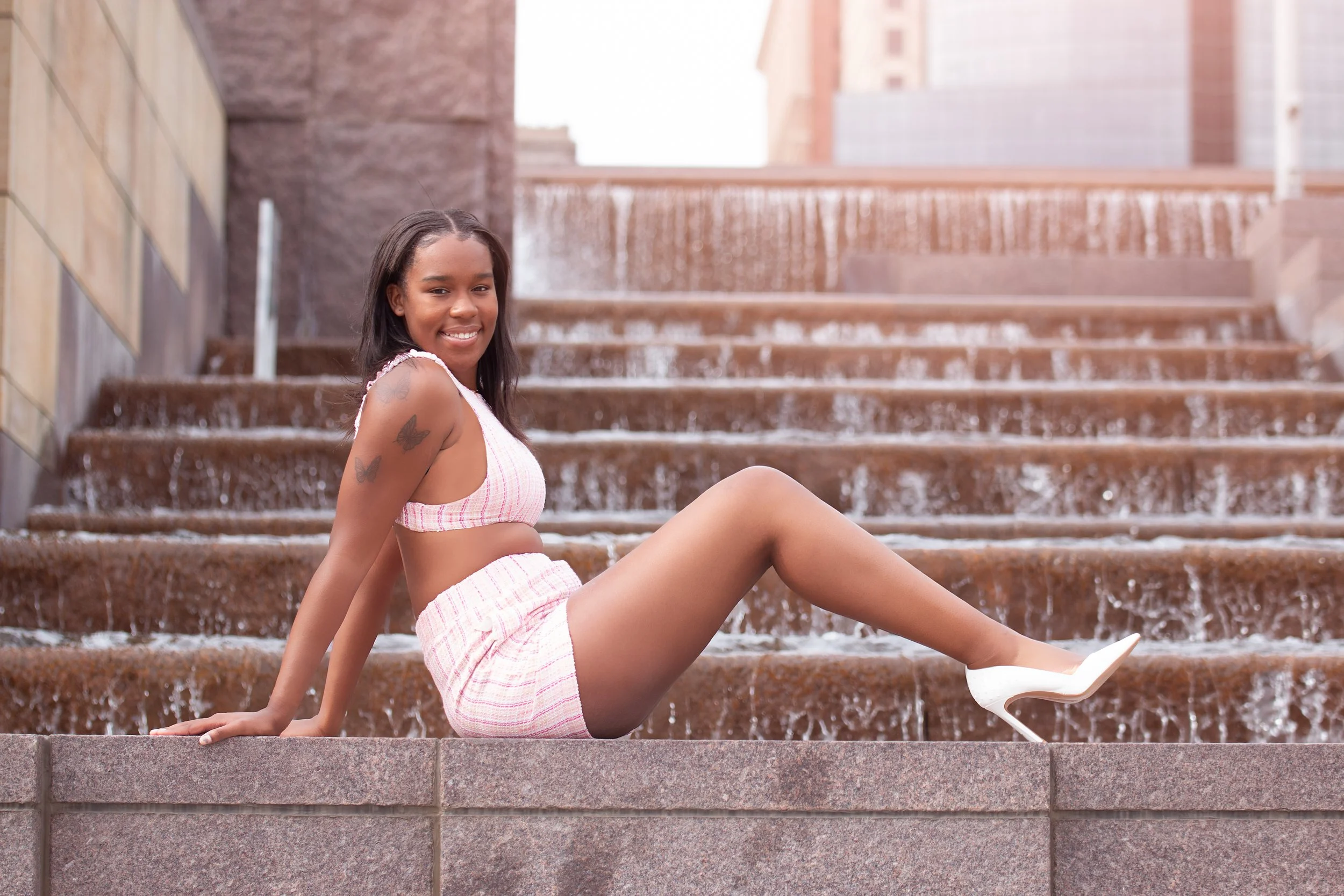 Creative senior portrait of girl posing on downtown water fountain steps in stylish pink outfit