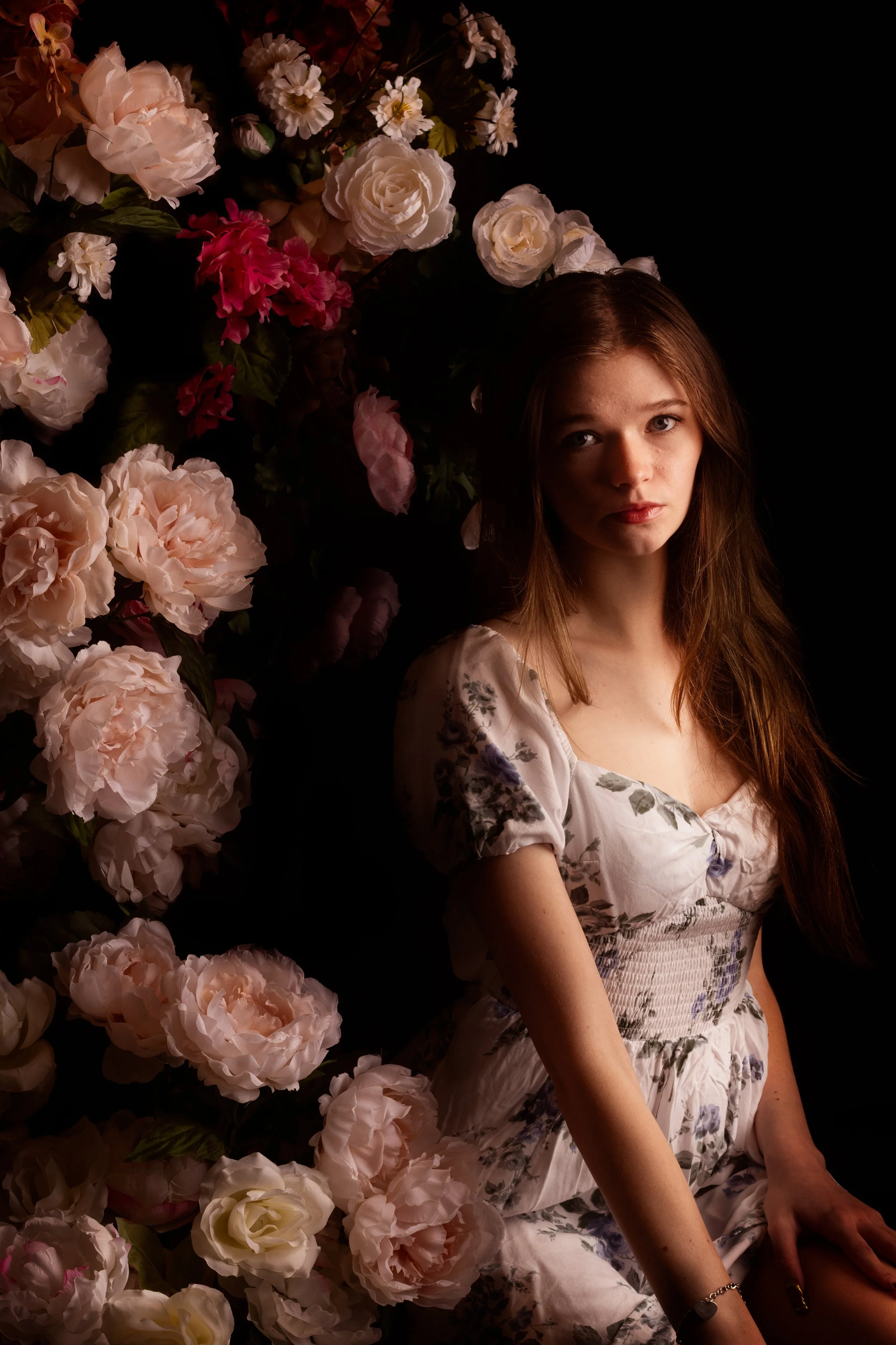 oung woman sitting in a gold frame surrounded by cascading flowers against a dark moody backdrop during a photography session at Say Yes to Jess studio in Cincinnati