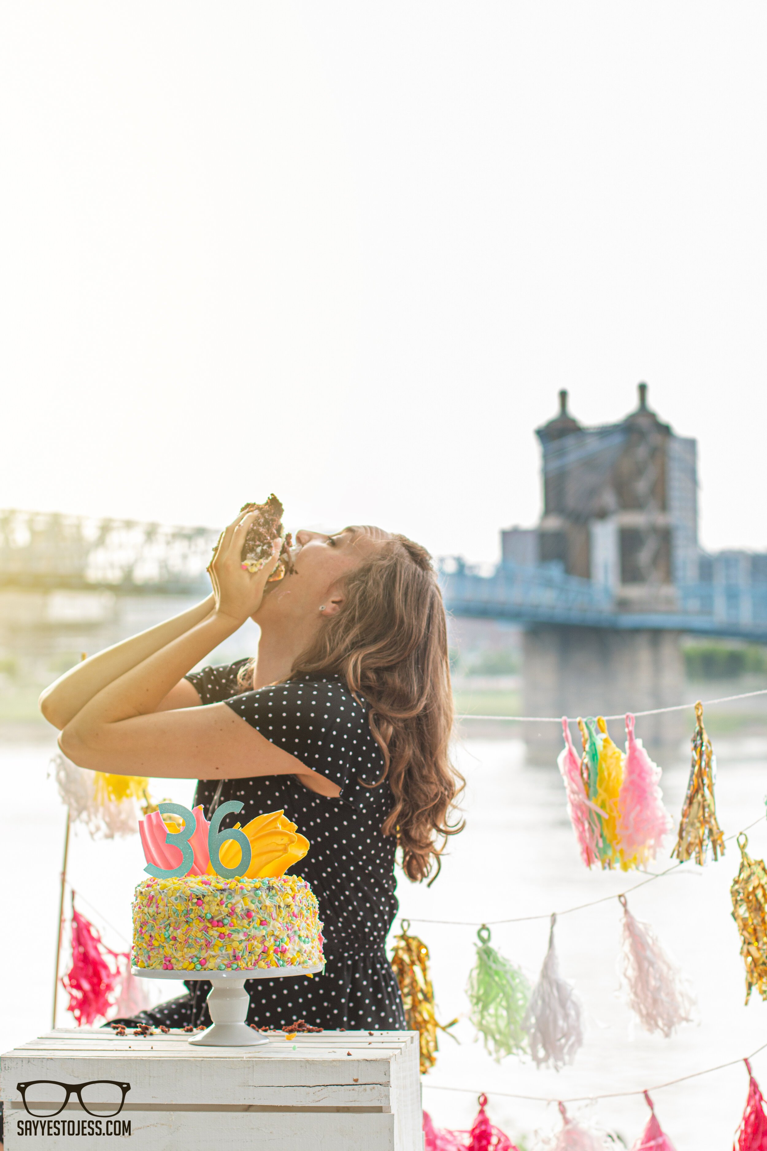 Woman eating a giant piece of birthday cake in front of the Roebling Bridge during a 36th birthday cake smash in Cincinnati