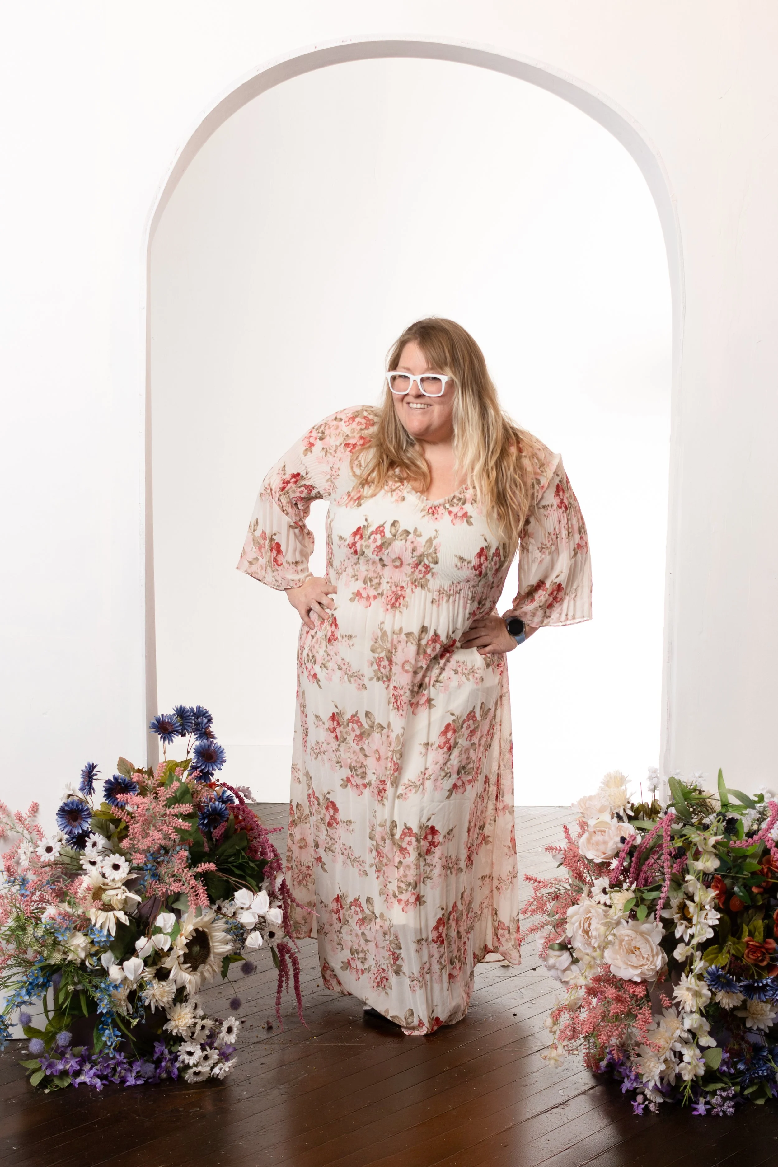 Cincinnati photographer Jess Summers standing in the white floral arch set wearing a floral dress at Say Yes to Jess studio for Mother's Day mini sessions