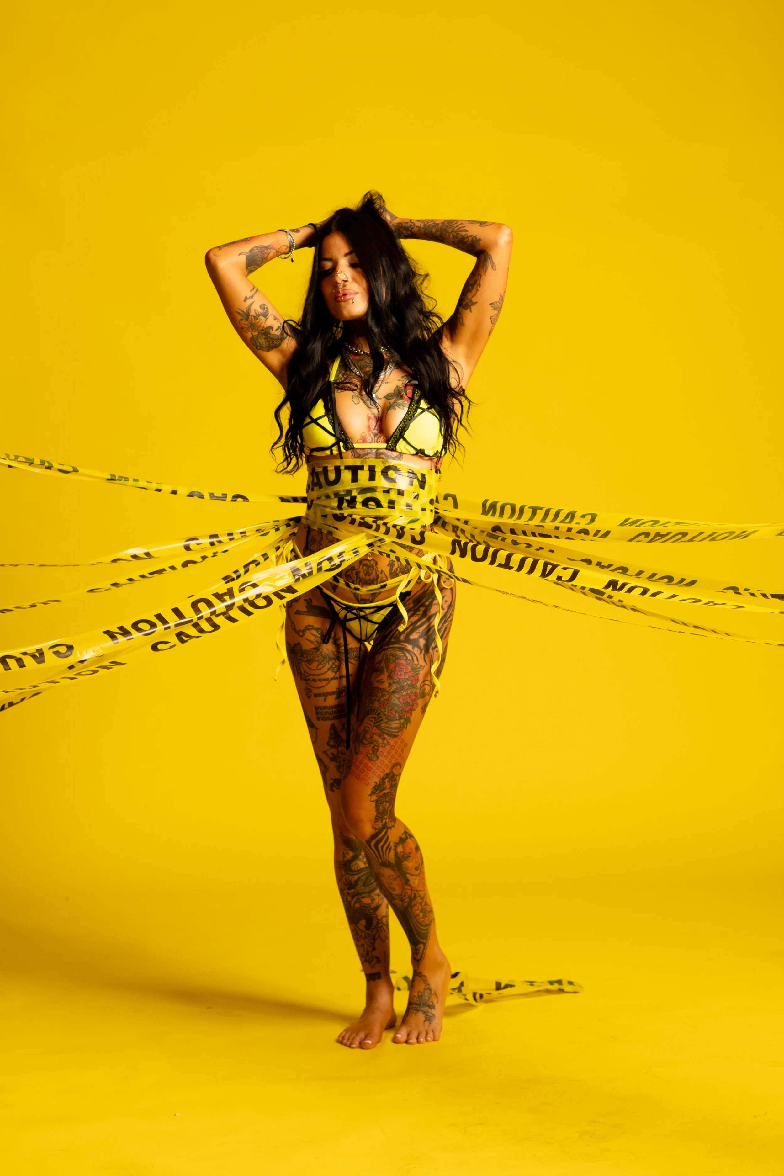 Bold editorial boudoir portrait of a tattooed woman wrapped in yellow caution tape at Say Yes to Jess studio in Cincinnati.