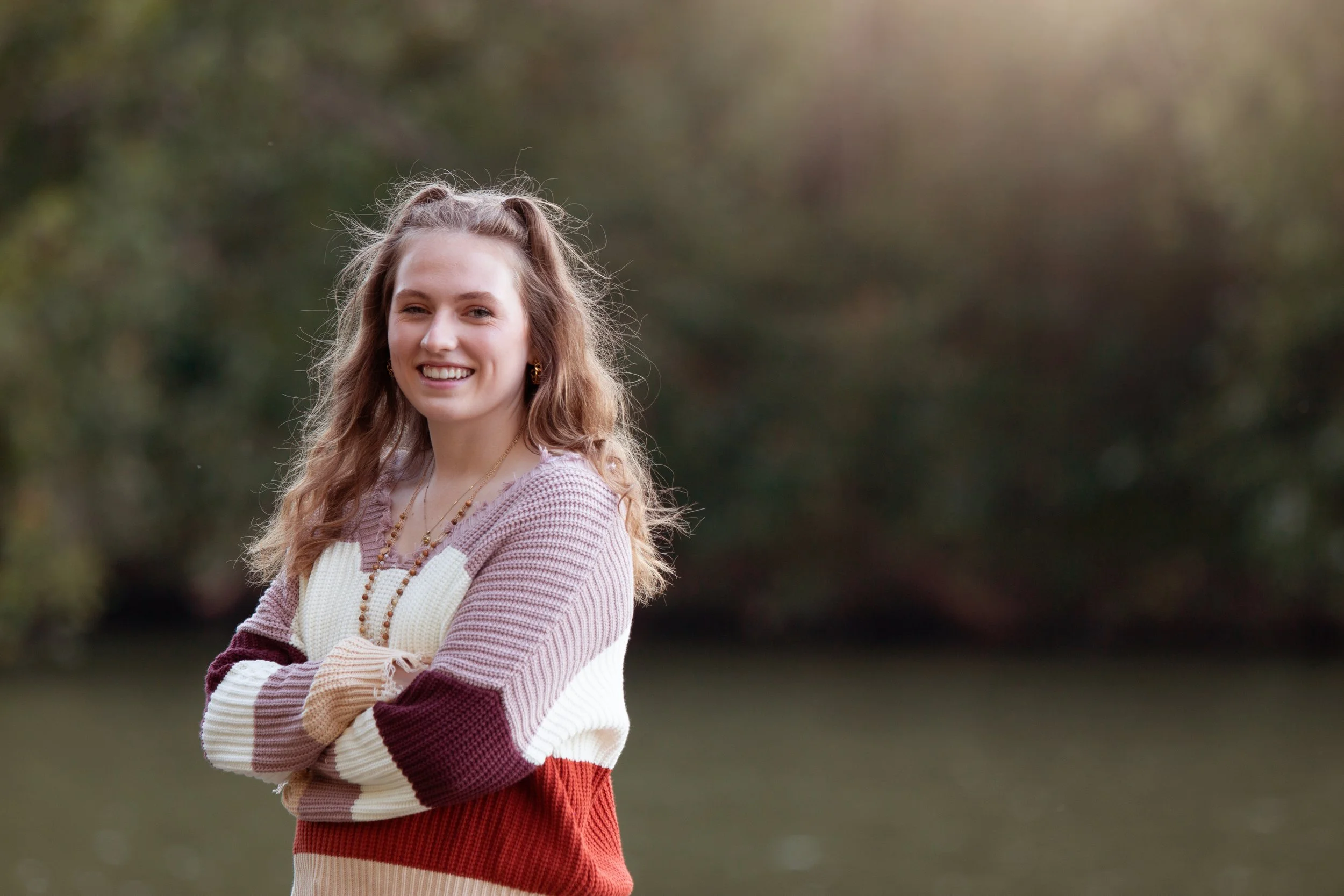 Outdoor senior pictures of smiling girl in colorful striped sweater during fall portrait session in Cincinnati
