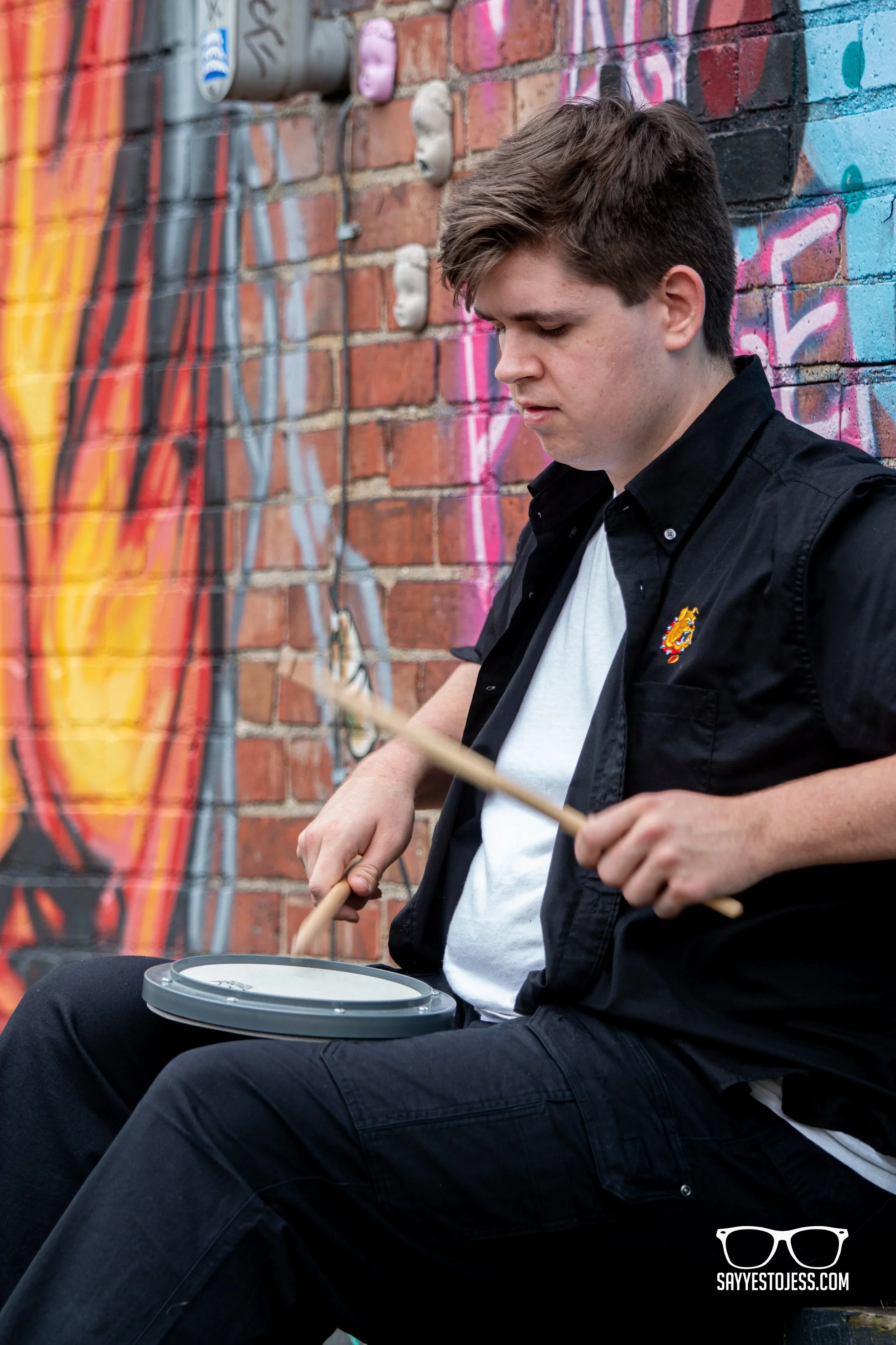 Male senior drumging while sitting aginst a wall for his senior photos