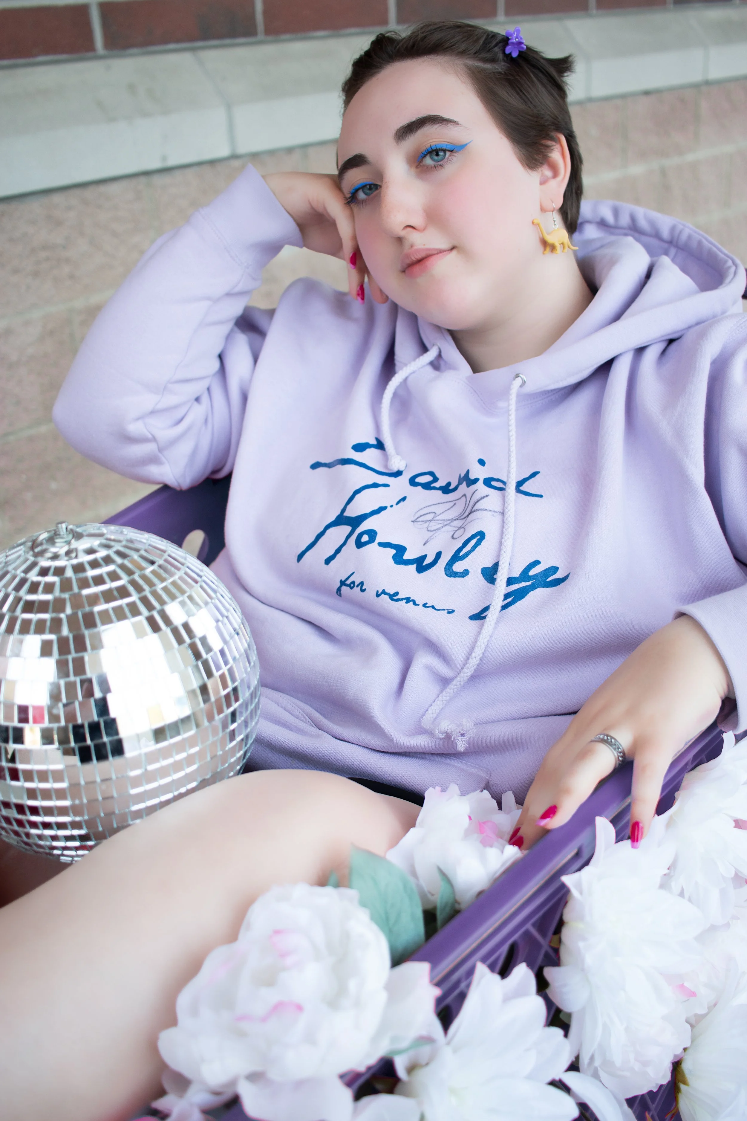 Close up senior portrait of girl in lavender hoodie with disco ball prop and bold accessories