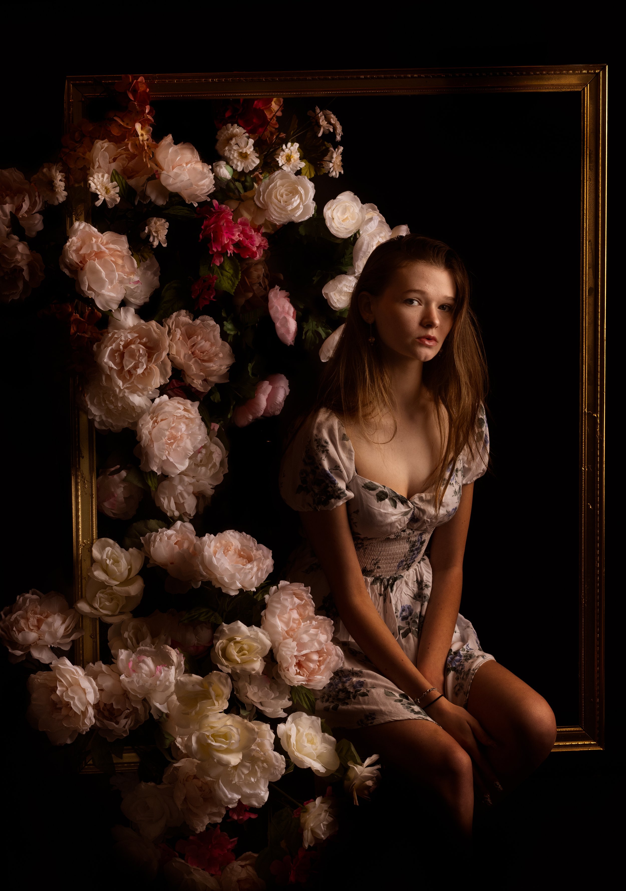 Moody dramatic portrait of a young woman surrounded by cascading roses and flowers in a gold frame set at Say Yes to Jess photography studio in Cincinnati Ohio