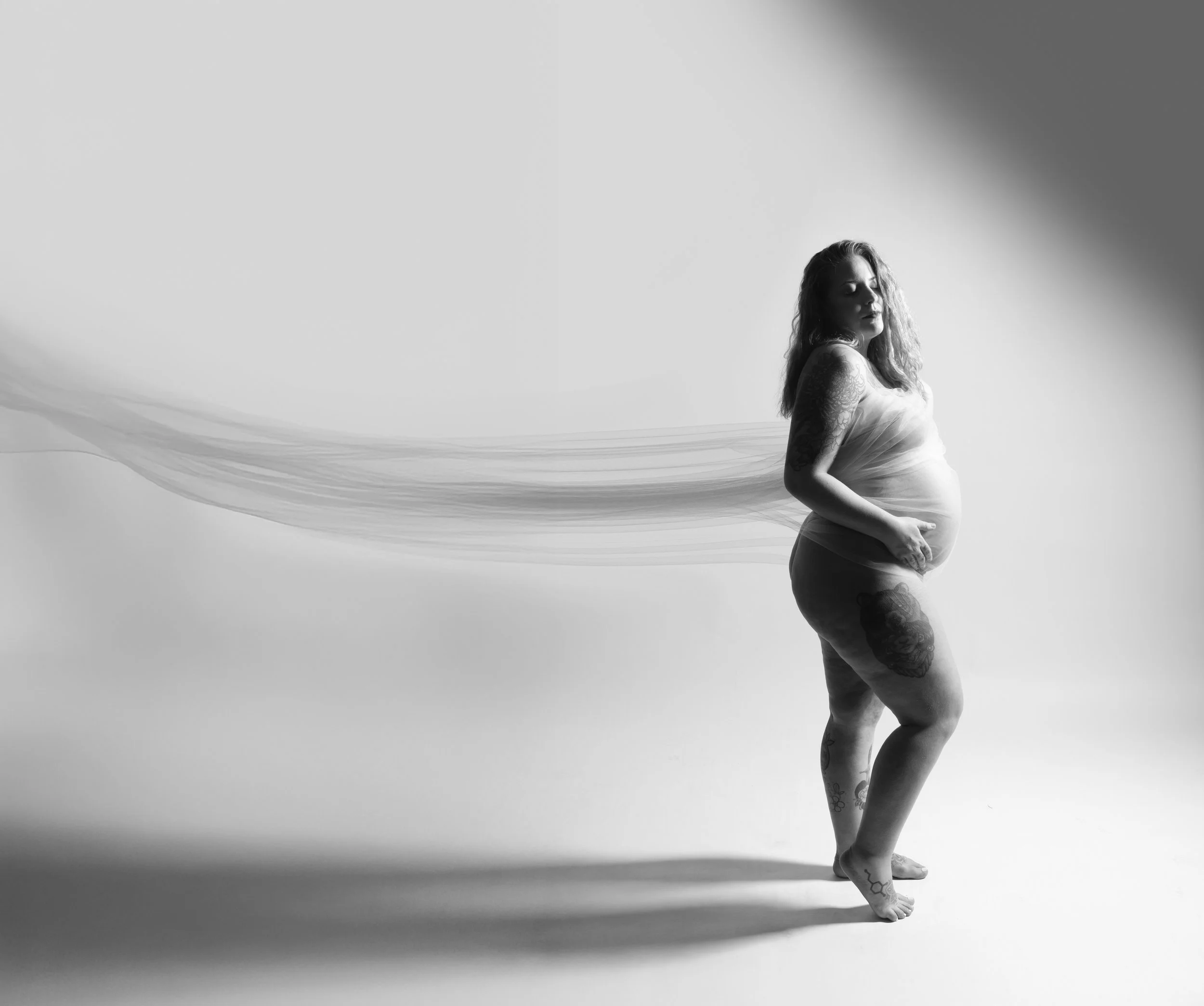 Black and white edgy maternity photo of tattooed pregnant woman draped in flowing sheer fabric in Cincinnati photography studio by Say Yes to Jess
