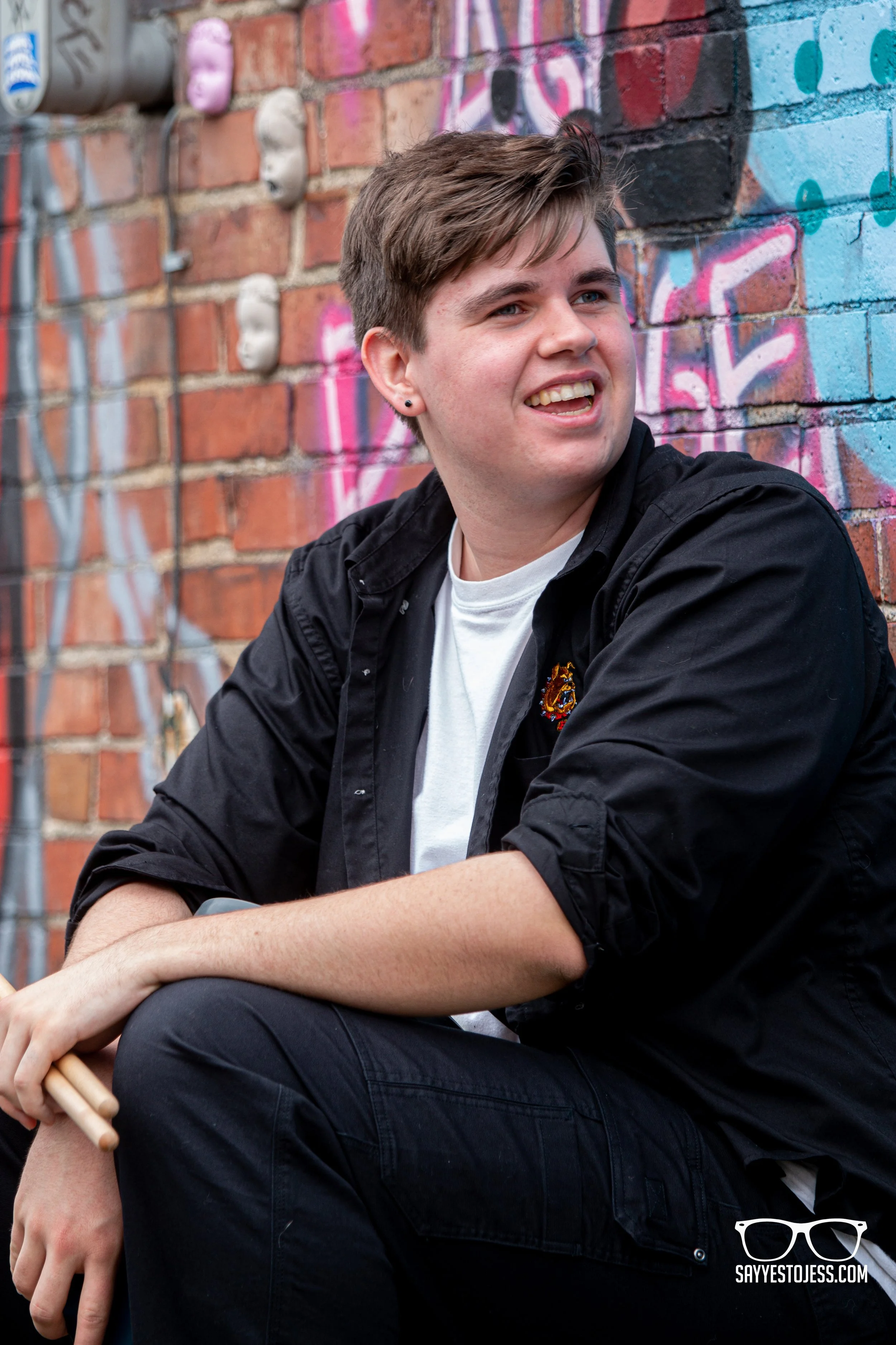 Young man smiles for his senior photos aginst a cool graffiti wall in northside ohio