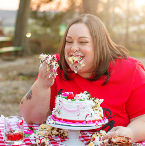Woman holding a smash cake with frosting on her face representing the inquire step for booking a cake smash session at Say Yes to Jess