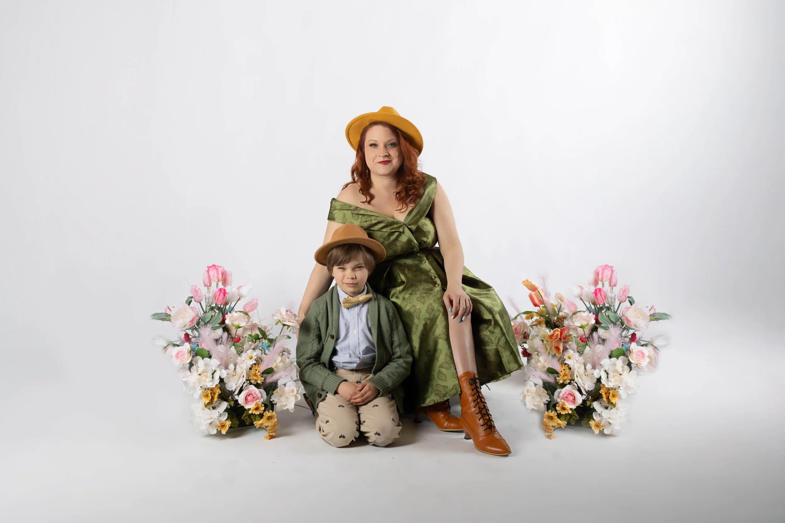 Mother and son in matching green outfits and mustard hats posing together surrounded by pink and white floral arrangements during a mommy and me photography session at Say Yes to Jess studio in Cincinnati