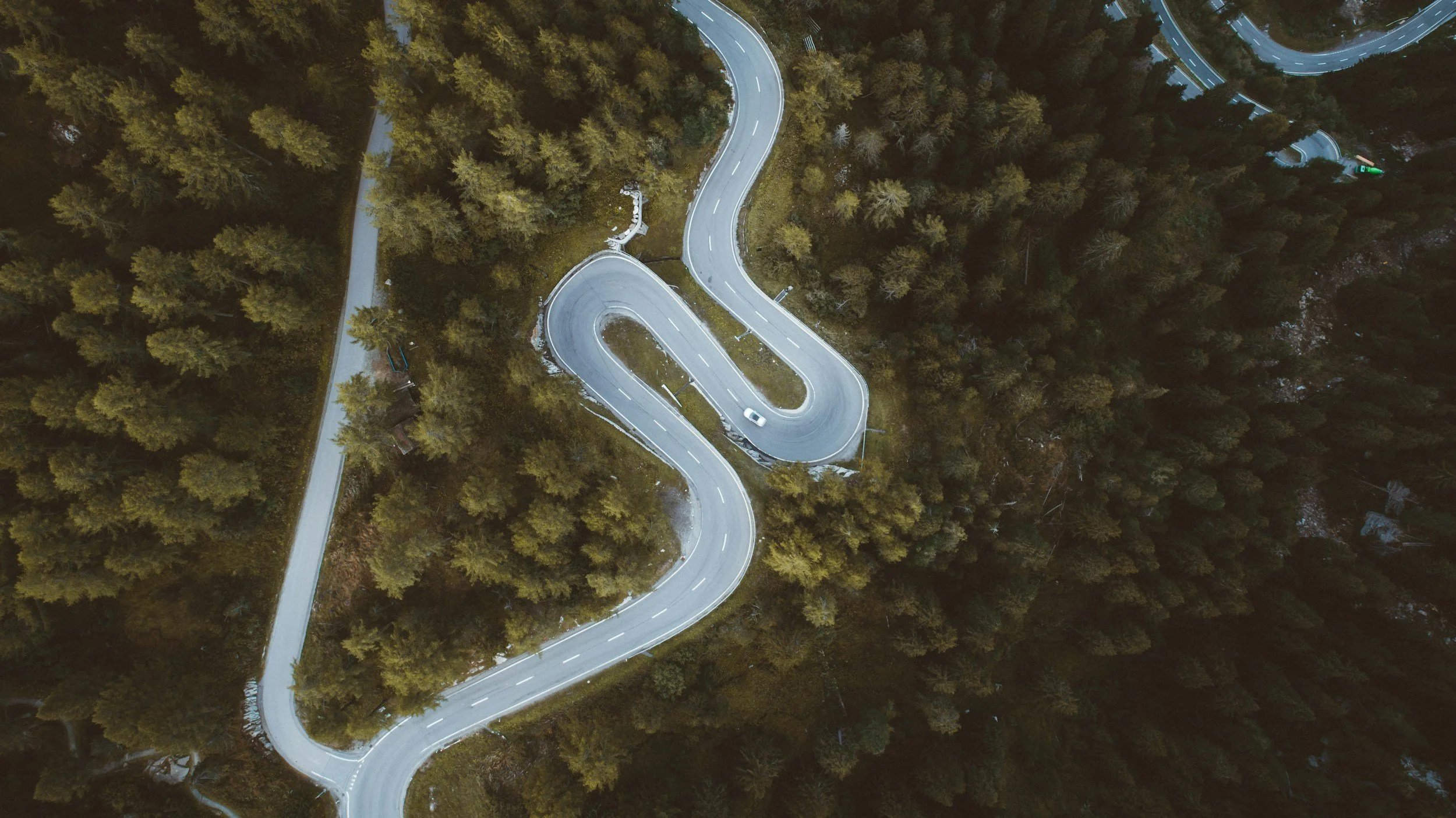 An aerial view of a winding mountain road through a forest, with a car driving on the road.