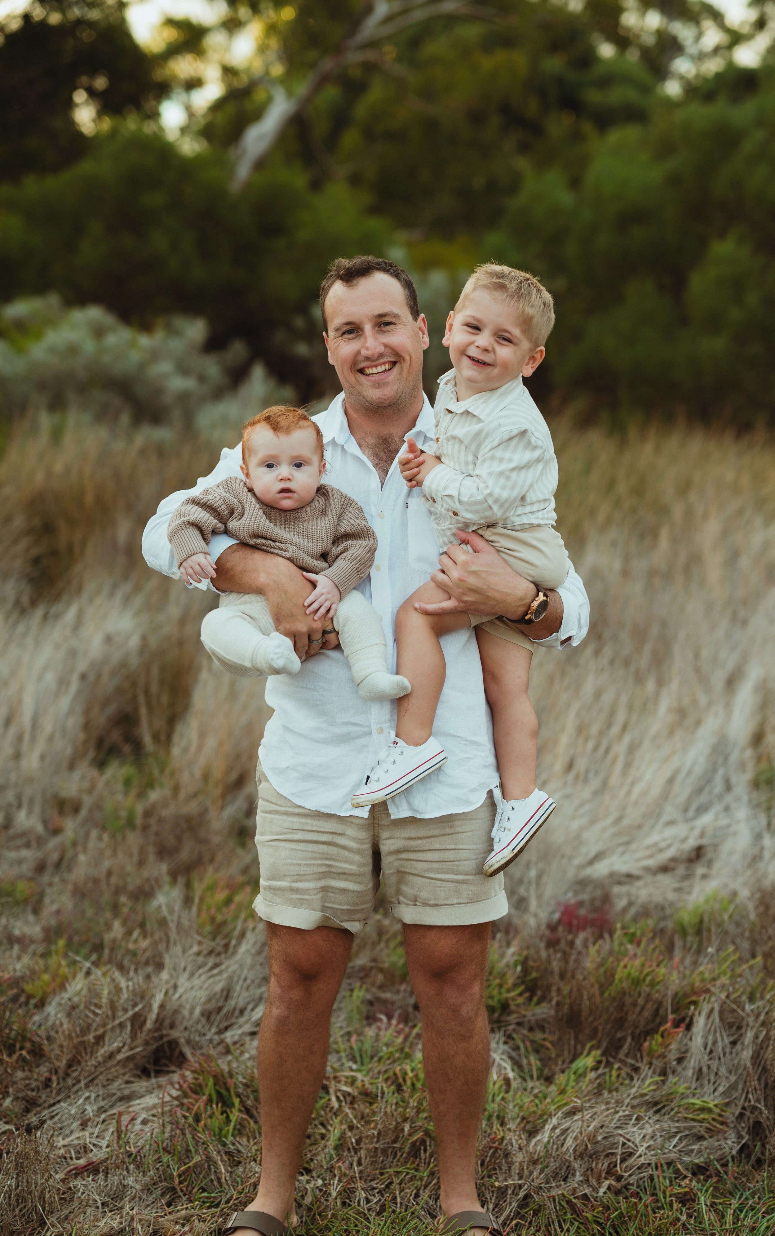 Man holding two children in a grassy field, smiling.