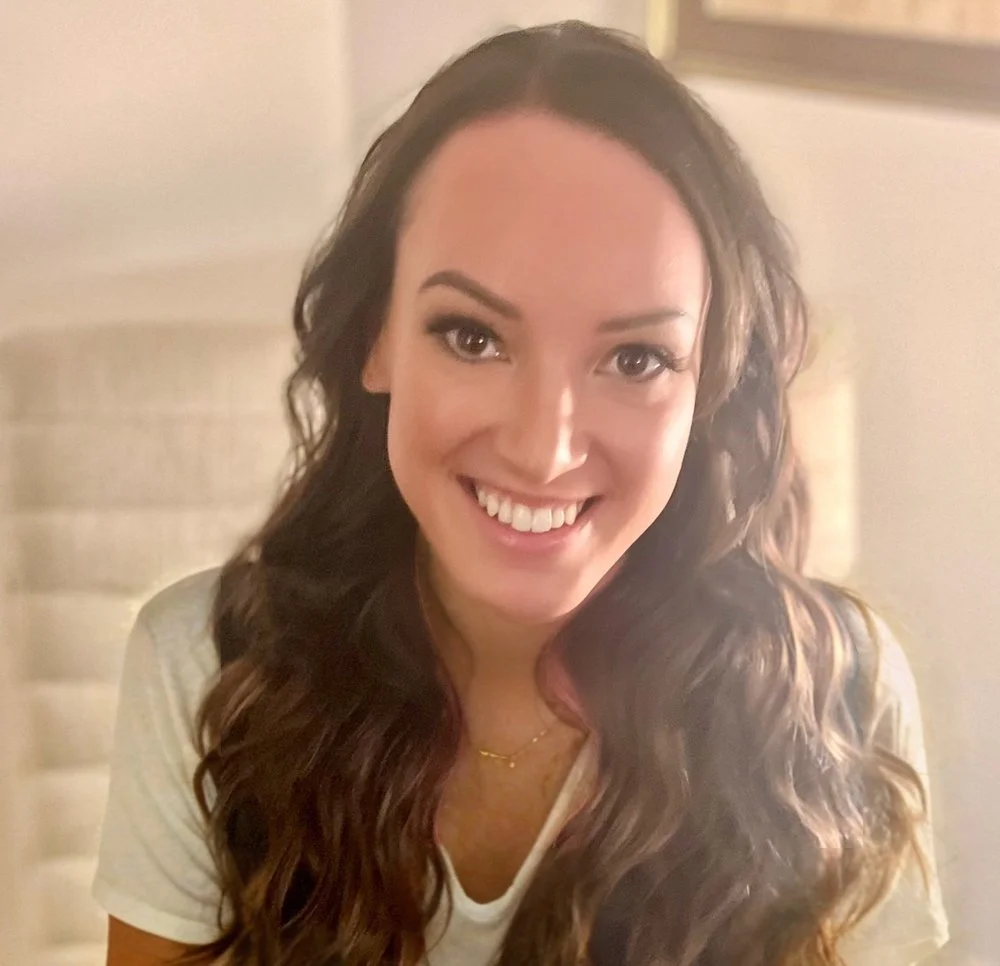 Smiling person with long wavy hair and a white shirt indoors.