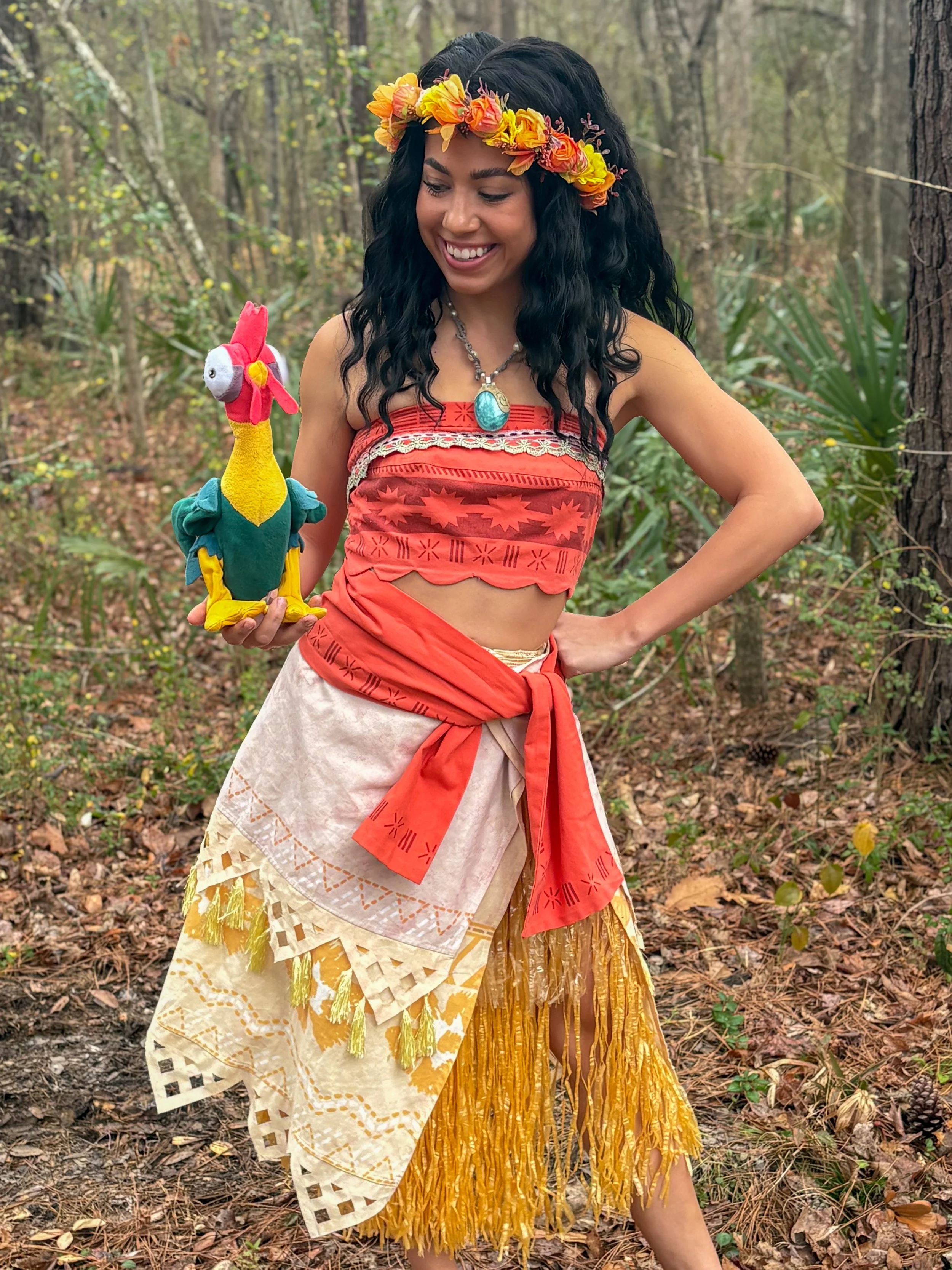 A woman in traditional Hawaiian attire standing on a beach with the ocean in the background.