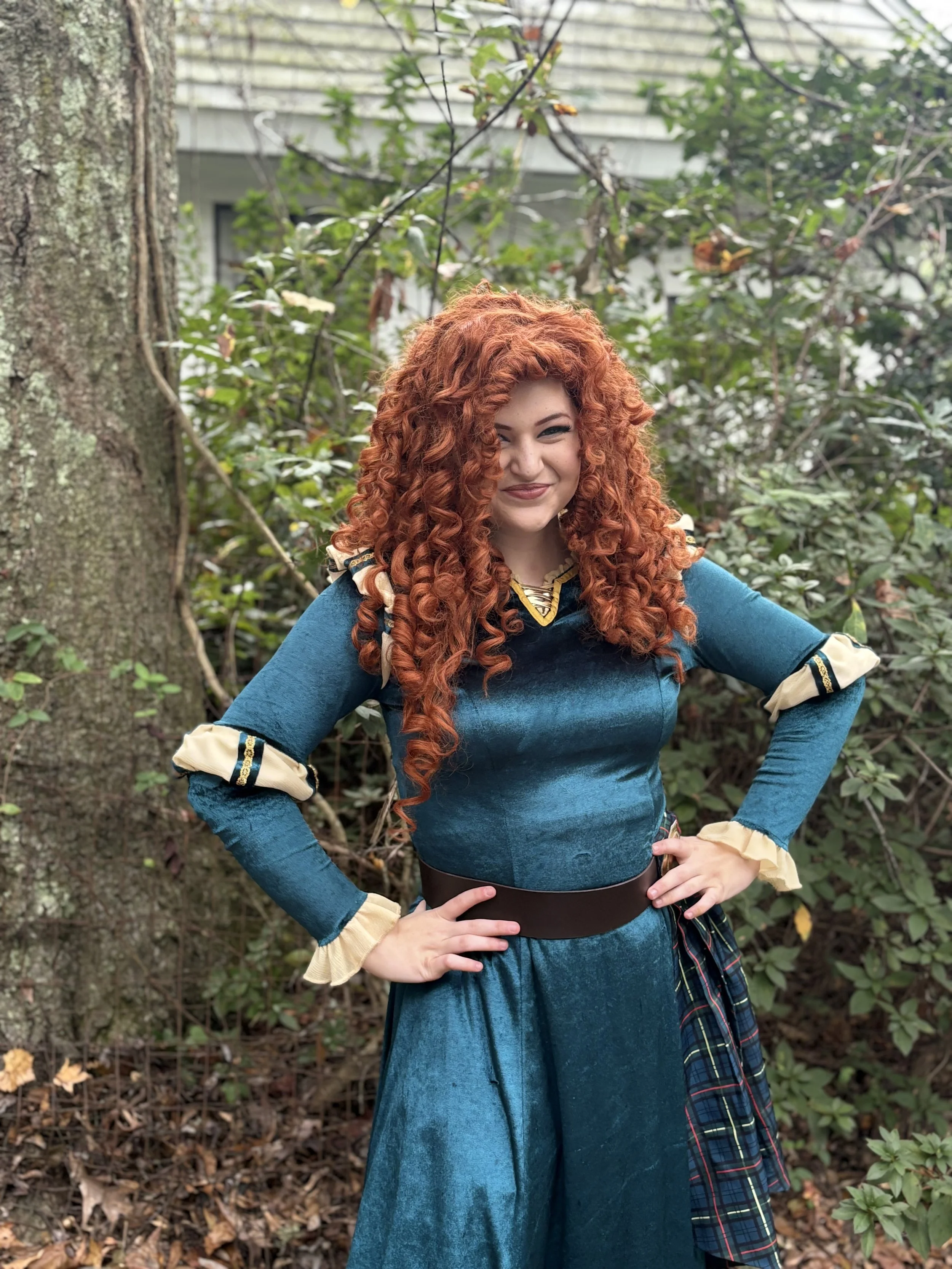 A woman dressed as Merida from Disney's 'Brave' stands in a forest, aiming a bow and arrow with a confident expression.