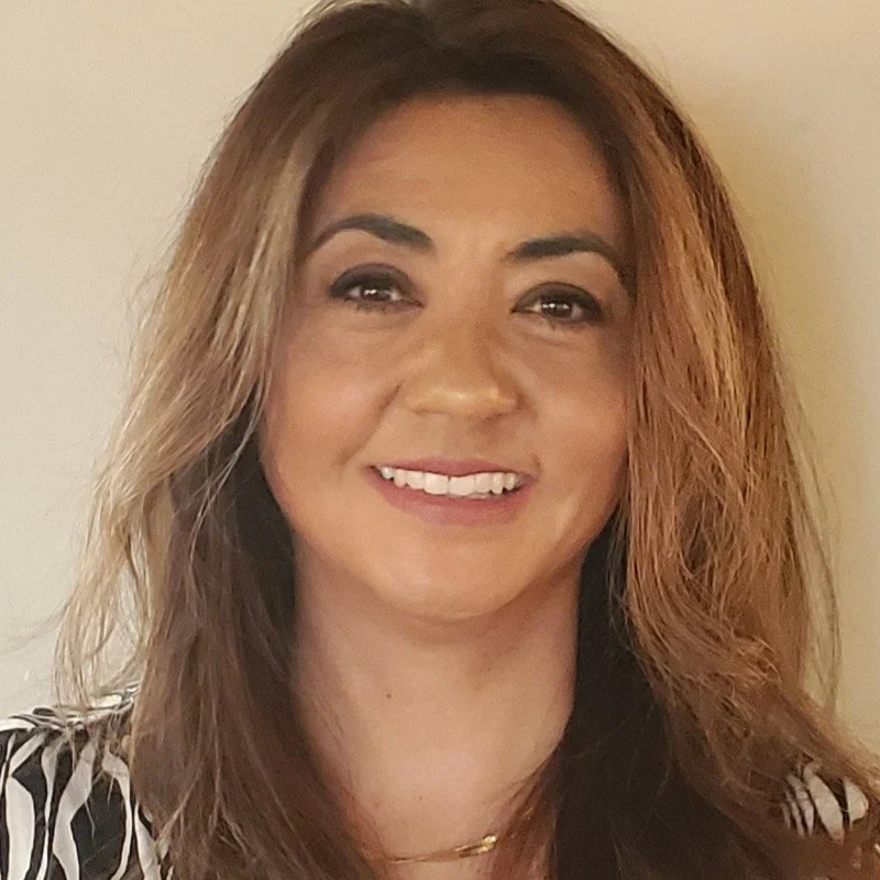 A woman smiling with shoulder-length, wavy, light brown hair against a plain background.