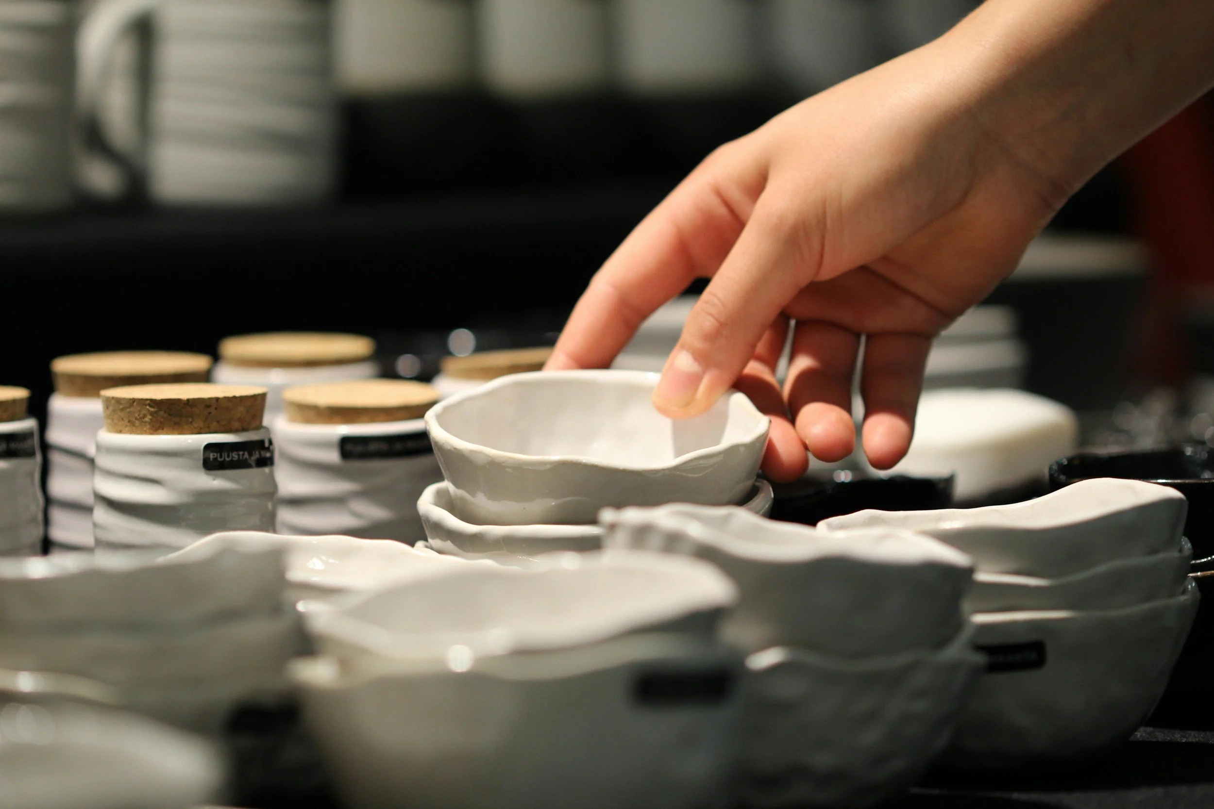 A person placing a ceramic cup on a shelf among other cups, with a blurred background.