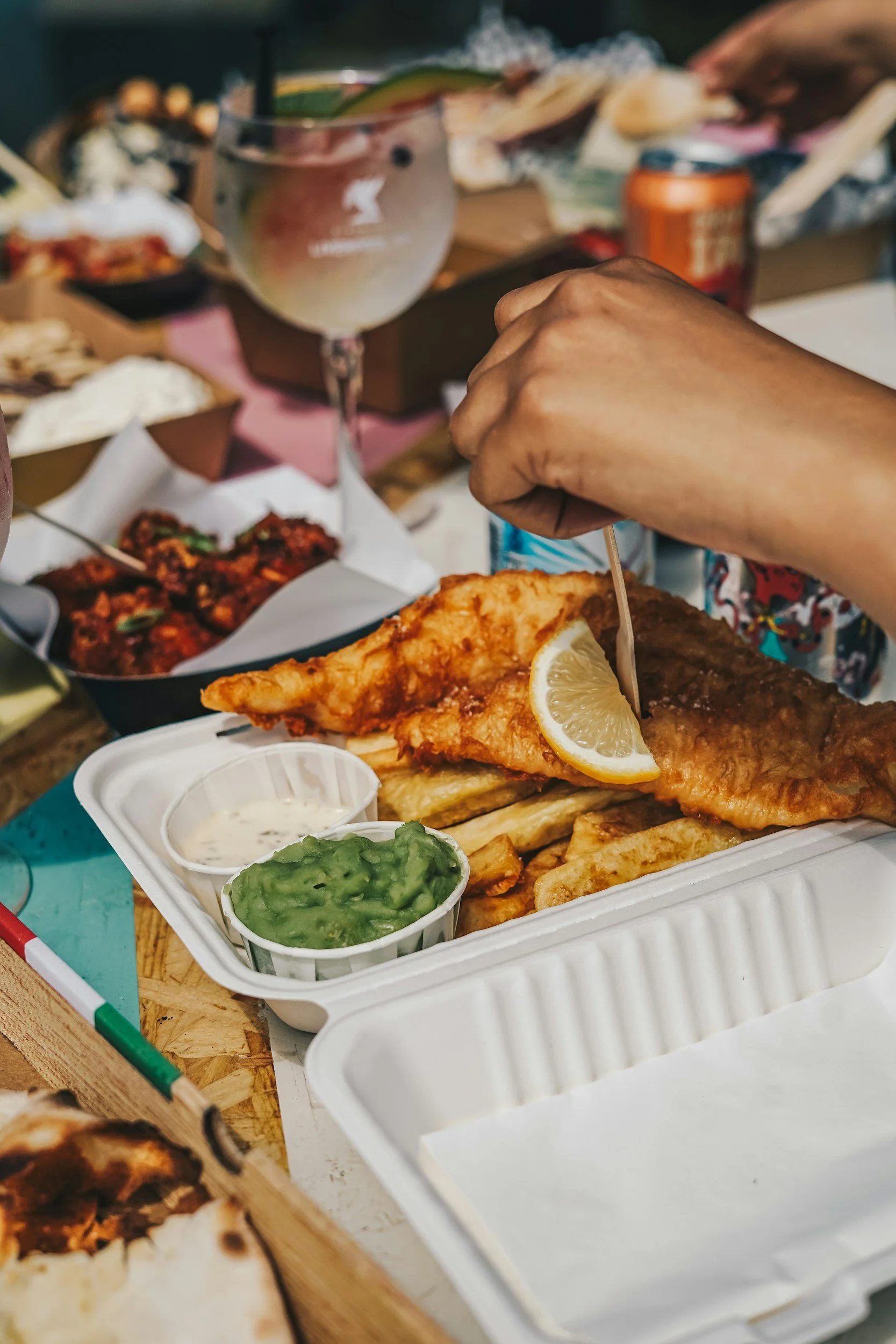 Fried fish fillet with lemon wedge on a white tray, accompanied by small containers of guacamole and sour cream, at a food gathering.