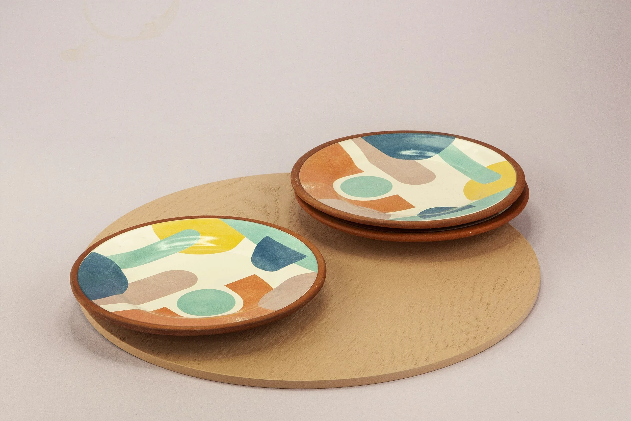 Colorful ceramic plates with abstract geometric designs stacked on a round wooden board.