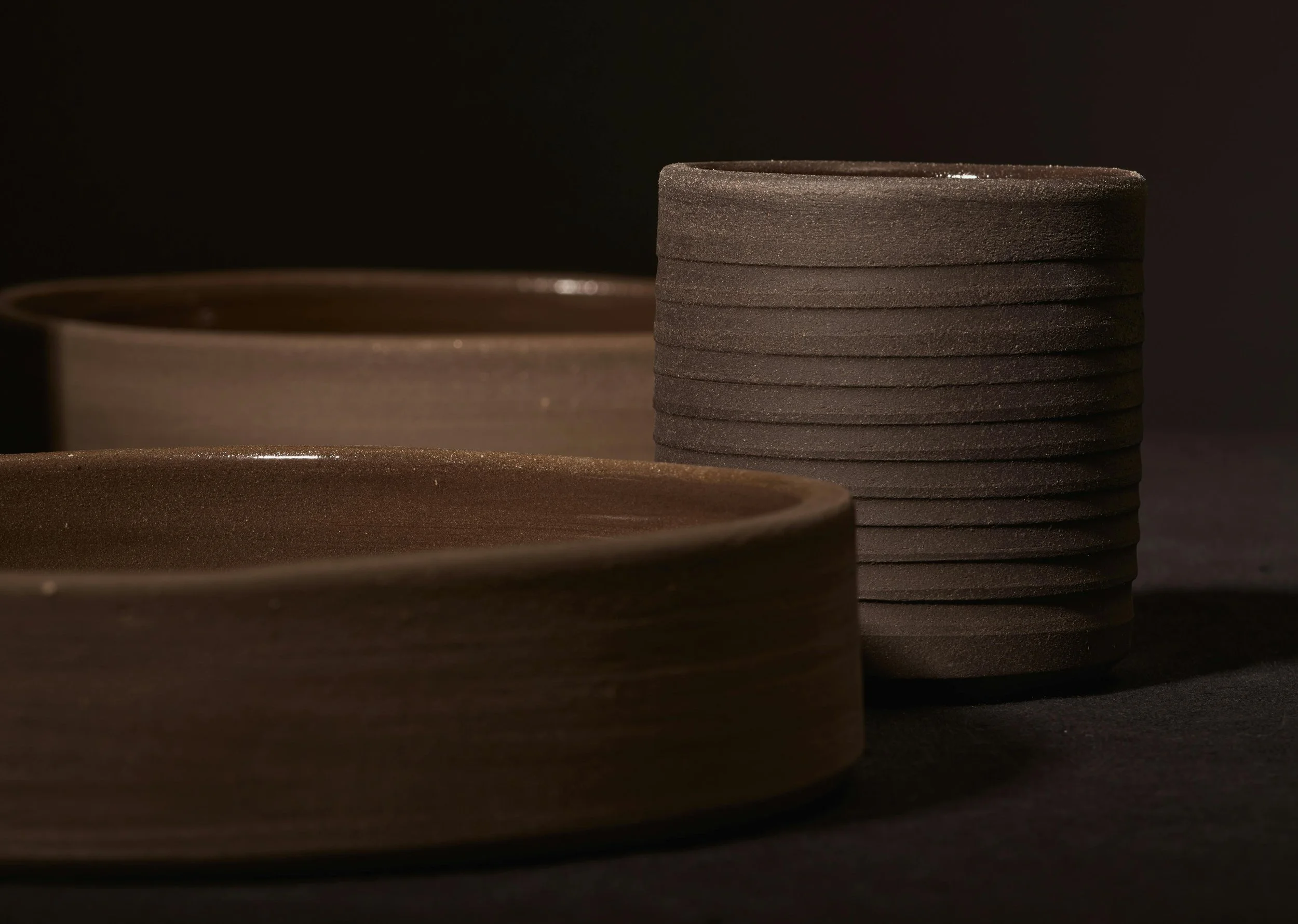 Close-up of stacked dark brown ceramic plates and bowls on a black background.