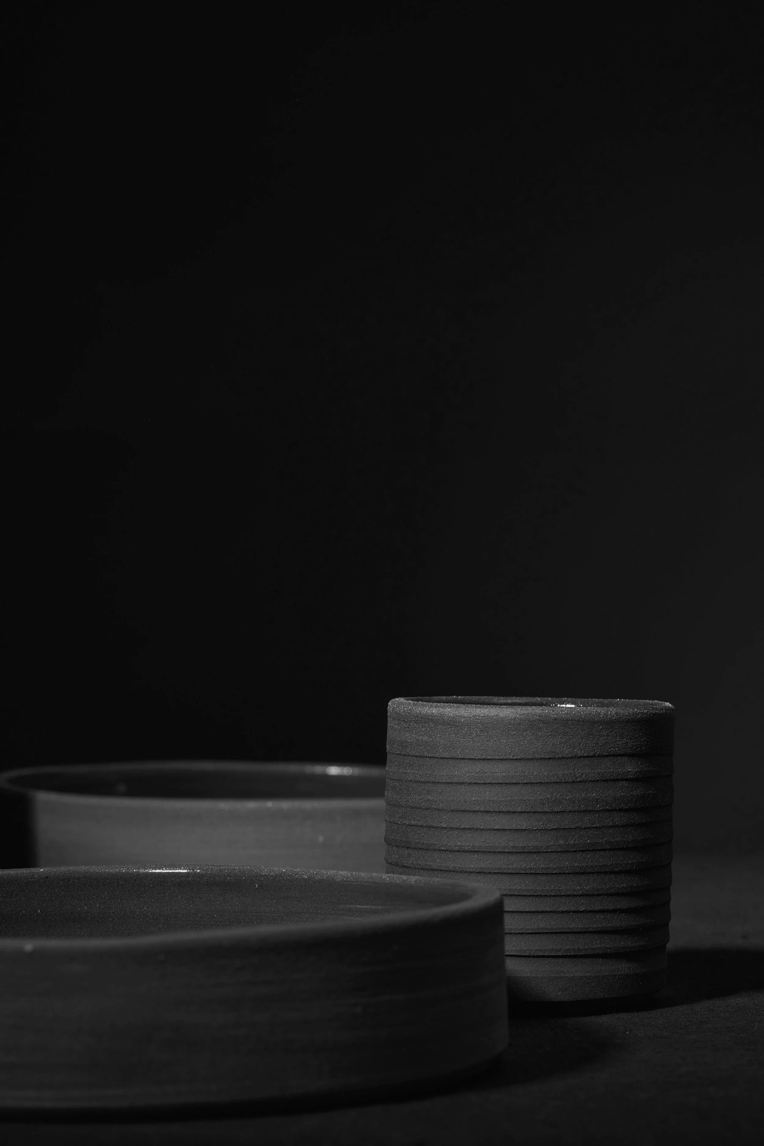 Stacks of black ceramic plates and bowls on a dark surface with a dark background.