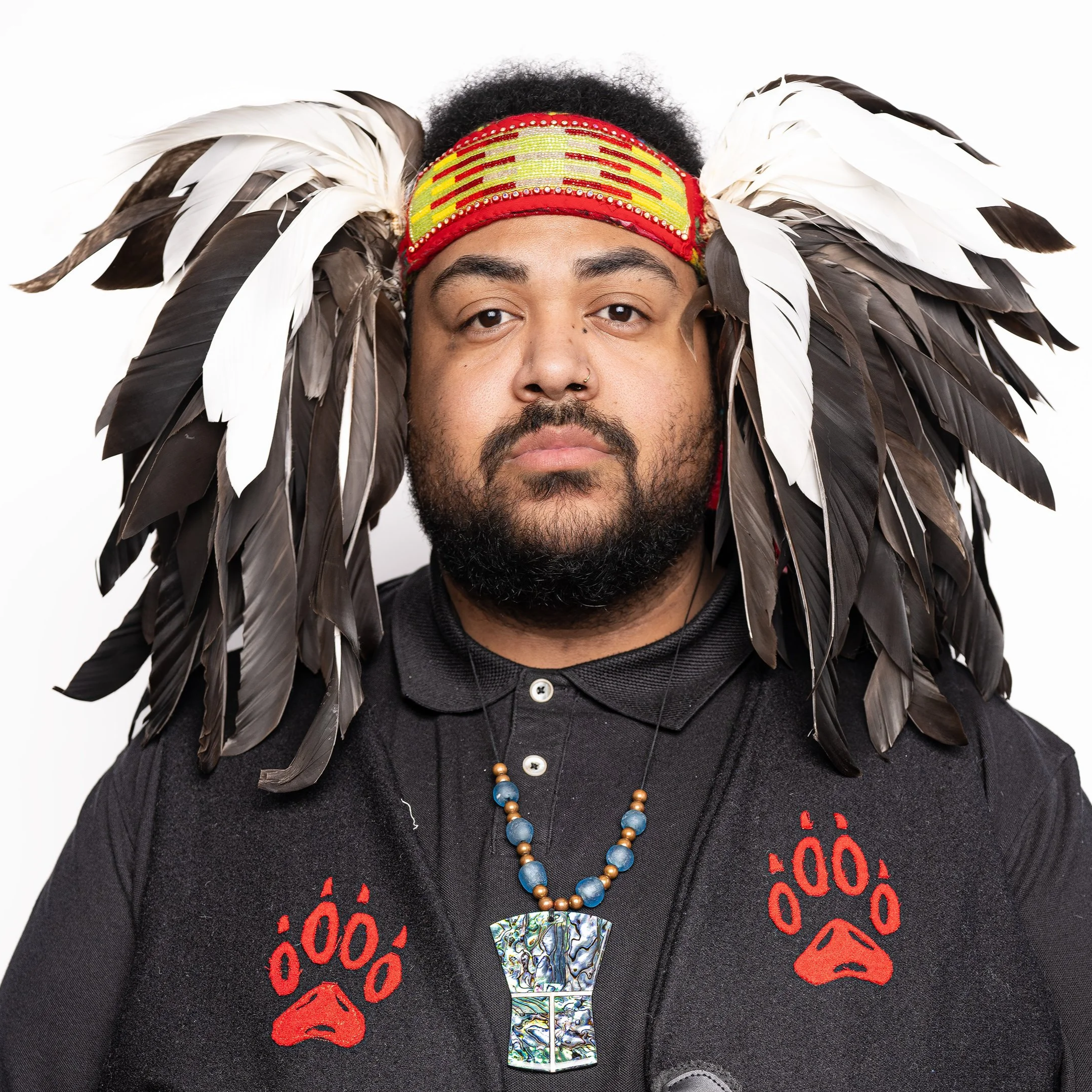Nicholas Kofi serves on the Board of Language Teacher Toolbox, a non-profit society in British Columbia. Nicholas is pictured wearing a headband with feathers and holding a red drum.