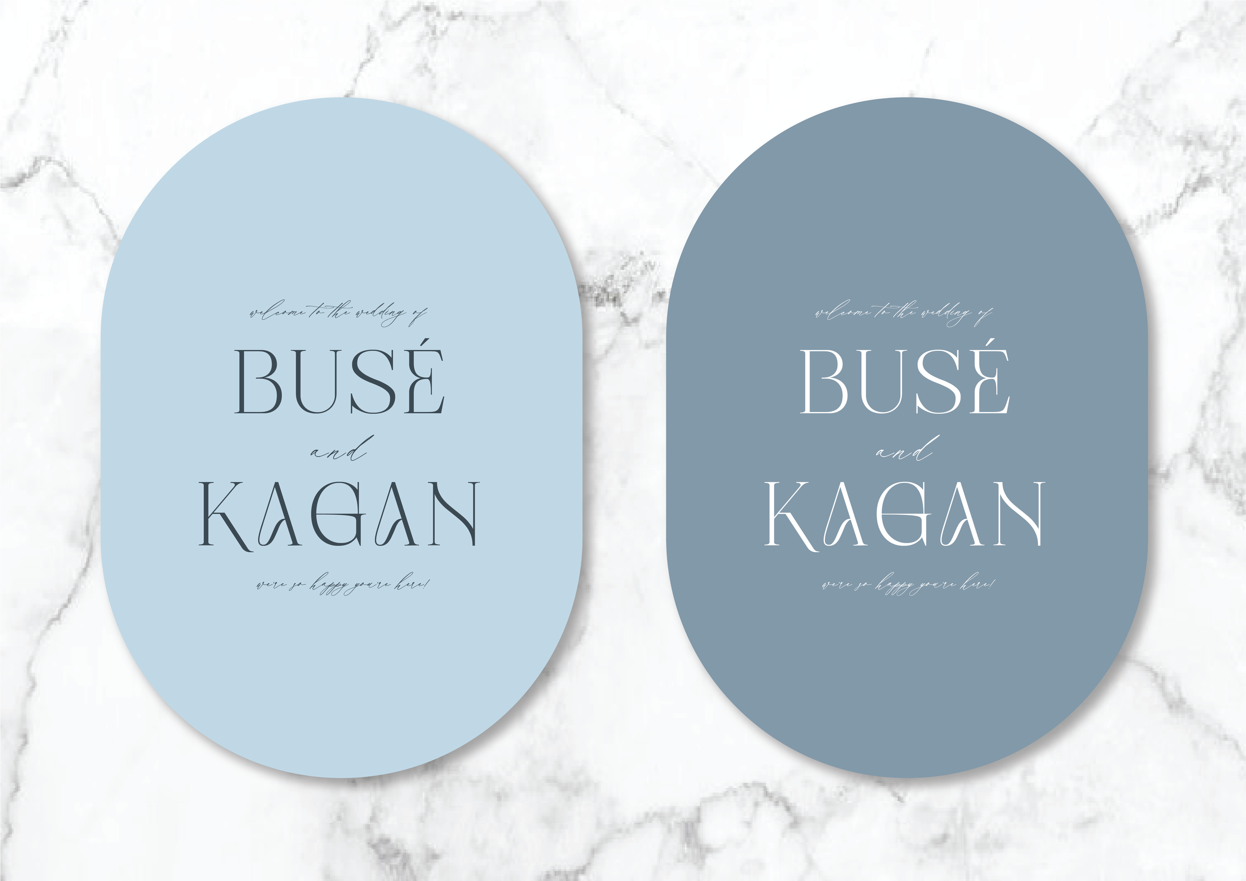 Two oval wedding invitations with text "Busé and Kagan" in elegant script, one in light blue and the other in slate gray, set against a marble background.