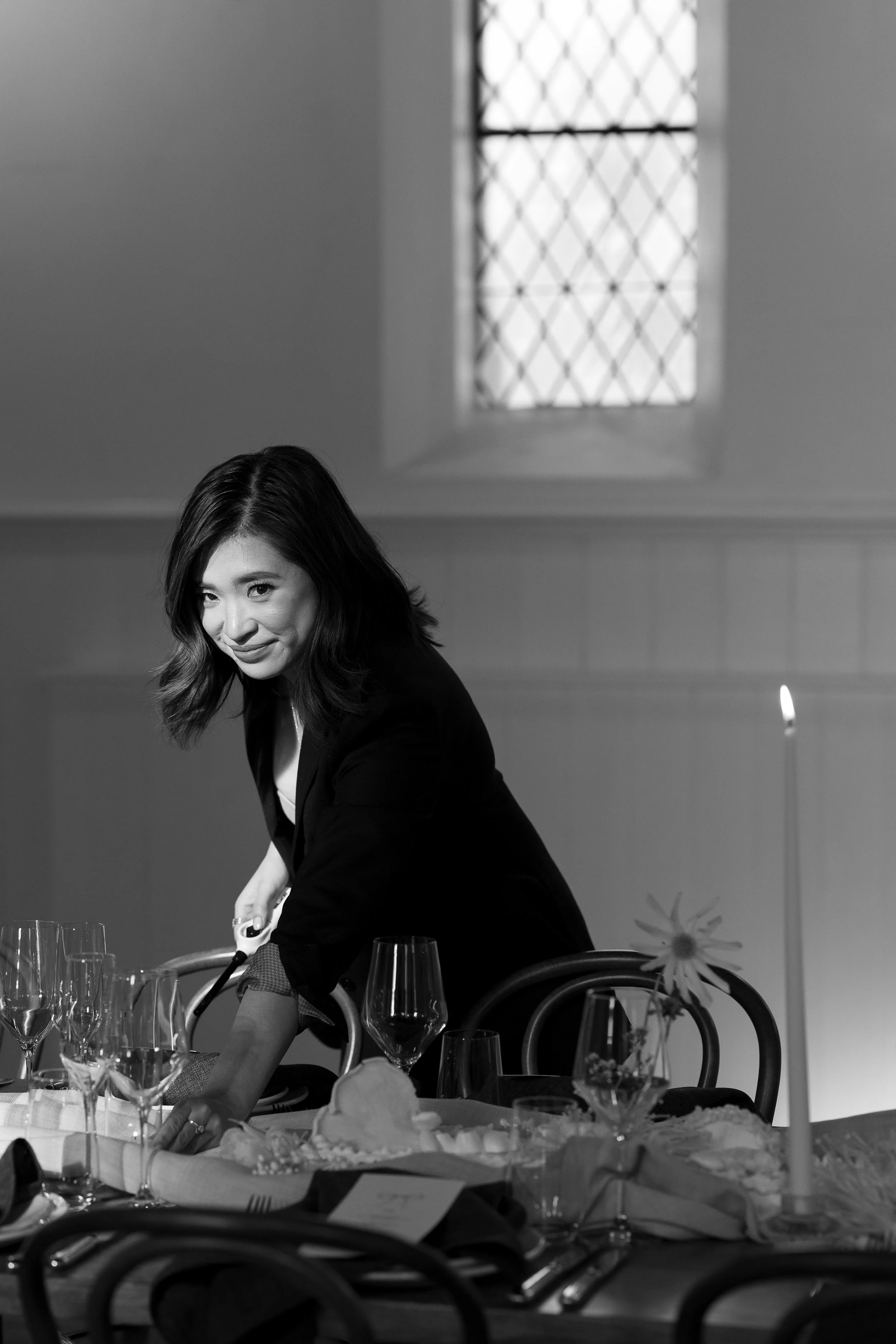 Woman setting a table with elegant glassware and folded napkins in a dimly lit room.