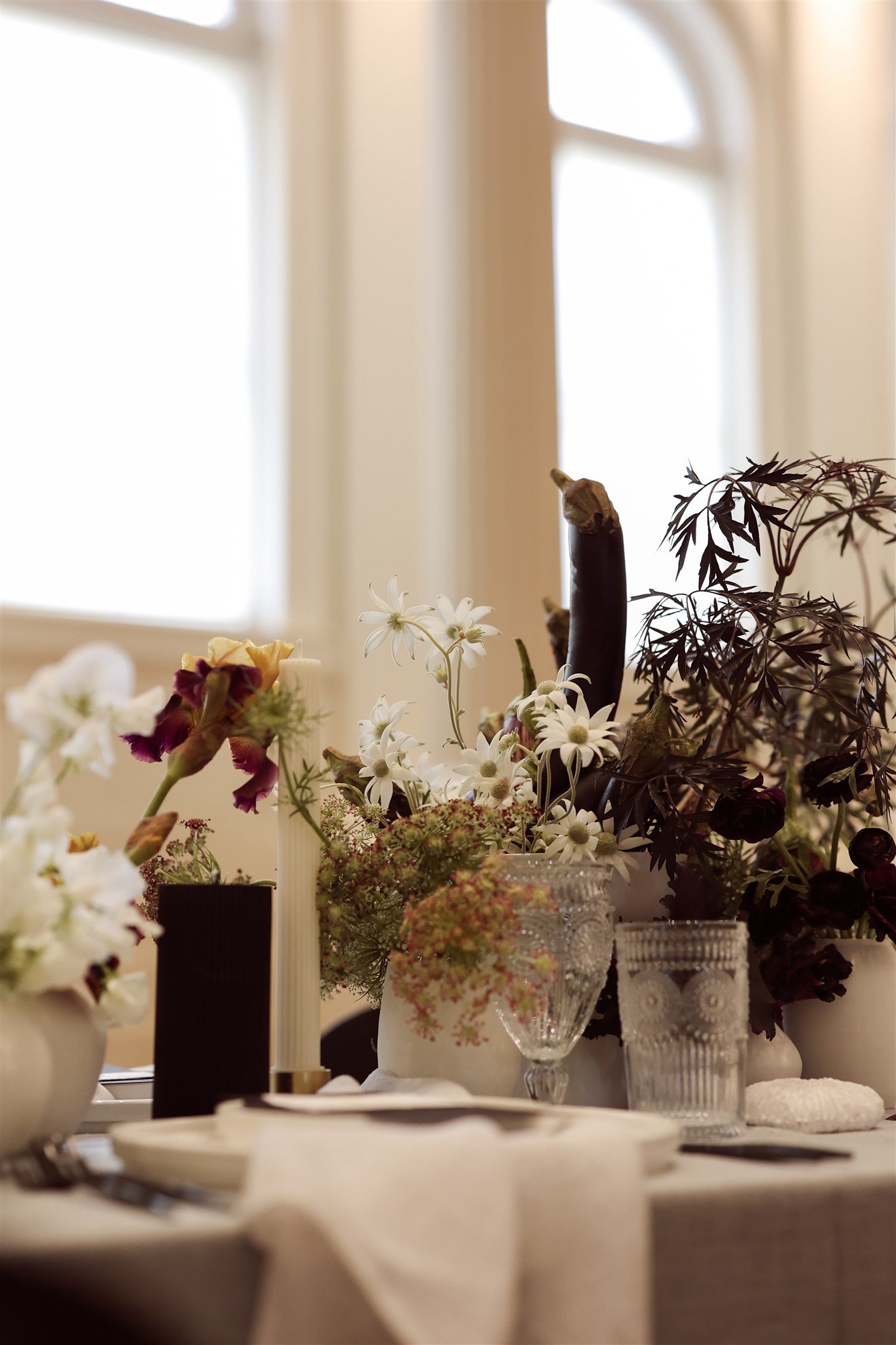 Elegant table setting with white and purple flowers, candle, crystal glassware, and napkins.