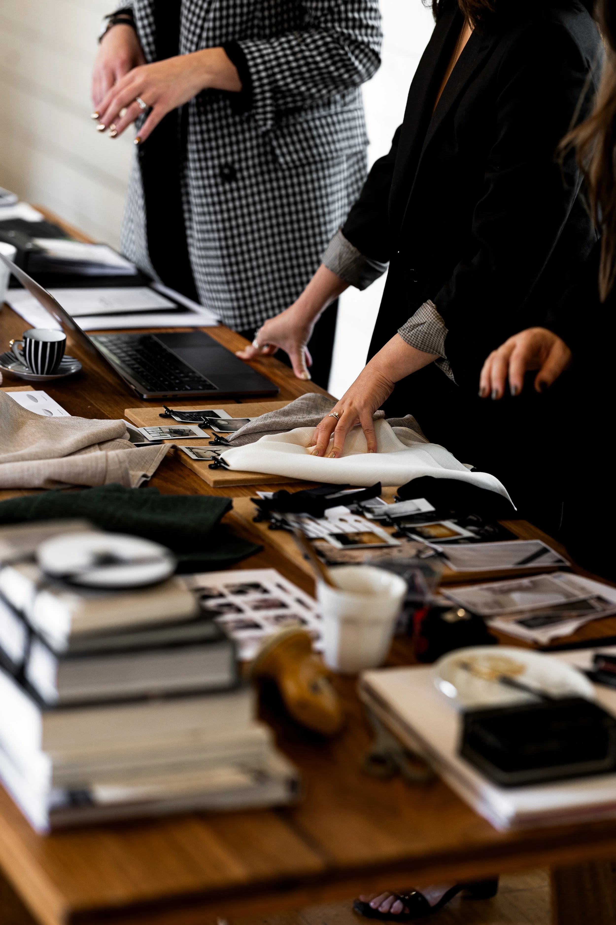People reviewing fabric swatches and design materials on a table, with a laptop and coffee cup present.