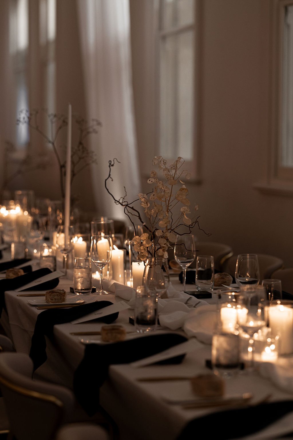 Elegantly set dining table with candles, glassware, and floral centerpieces, creating a warm, romantic ambiance.
