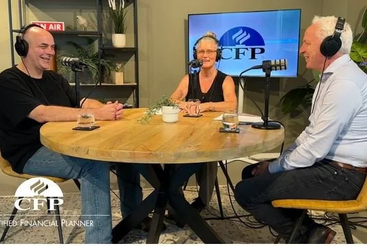 Drie mensen waaronder Willem Jonkers die aan een ronde tafel zitten en in een opname praten, met koptelefoons en microfoons.