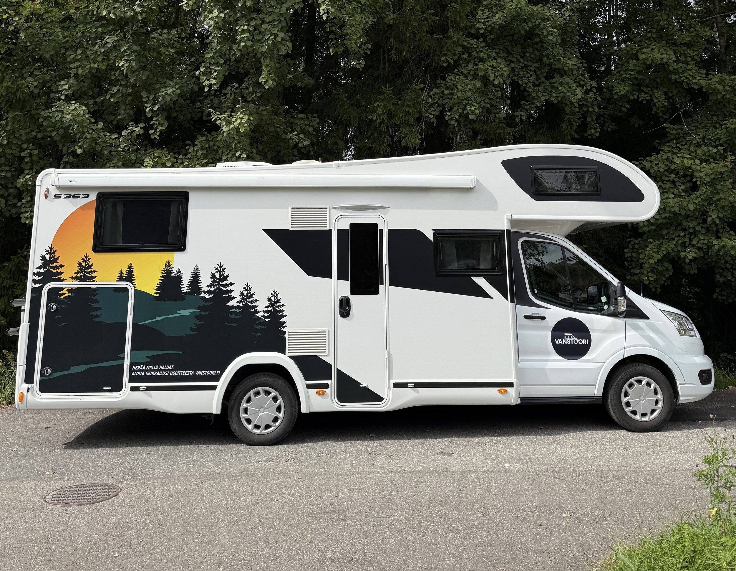 Matkailuauto parkissa tien varrella, metsää taustalla.