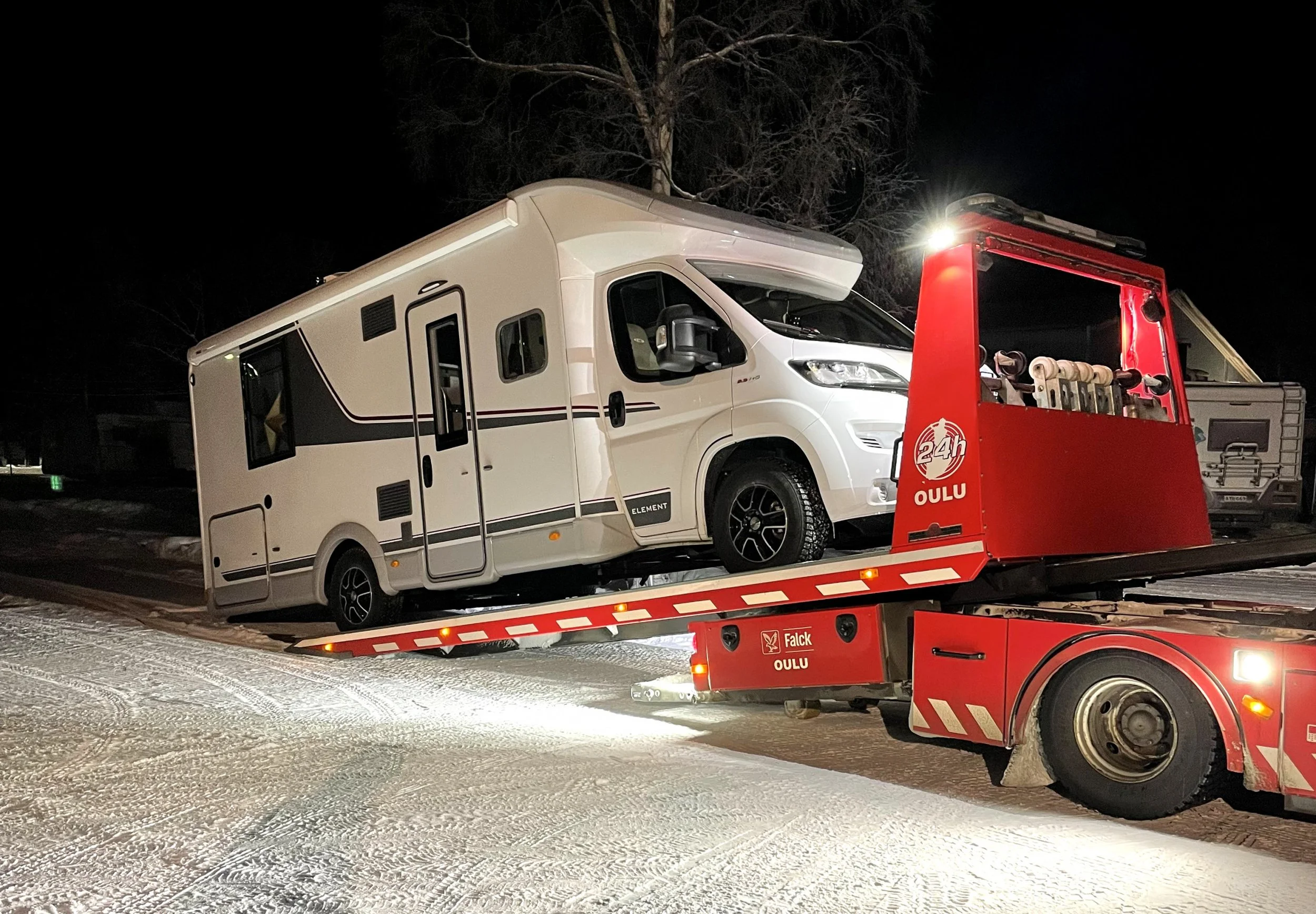 Retkeilyauto lastattu hinausautossa, lumisella tiellä yöllä.