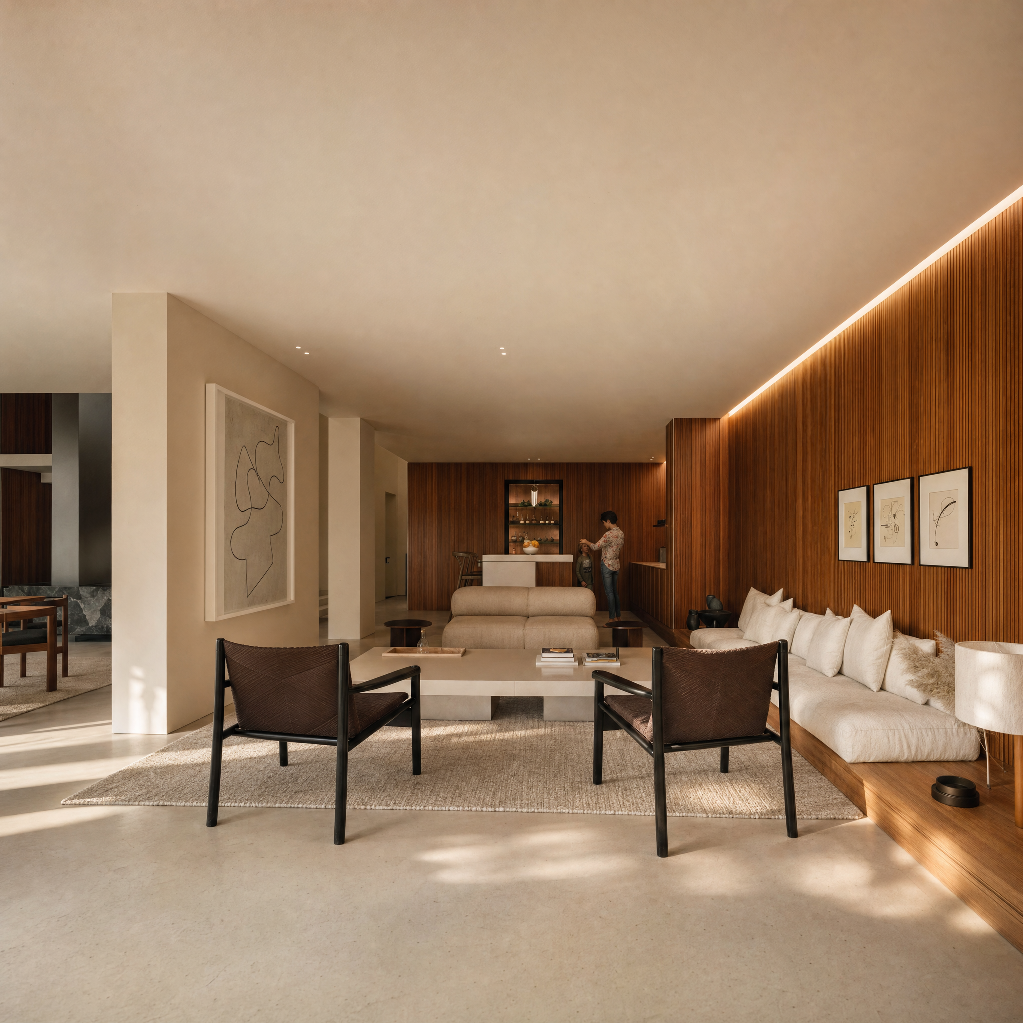 Modern living room with beige sofa, dark wood chairs, artwork on cream wall, wooden accent wall, and person with child near island.