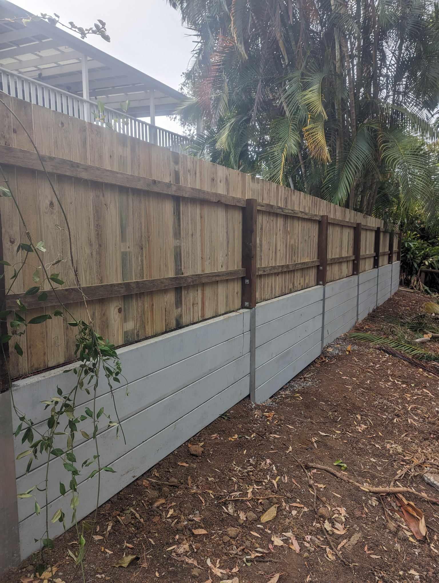 Wooden fence with concrete base near palm trees and house