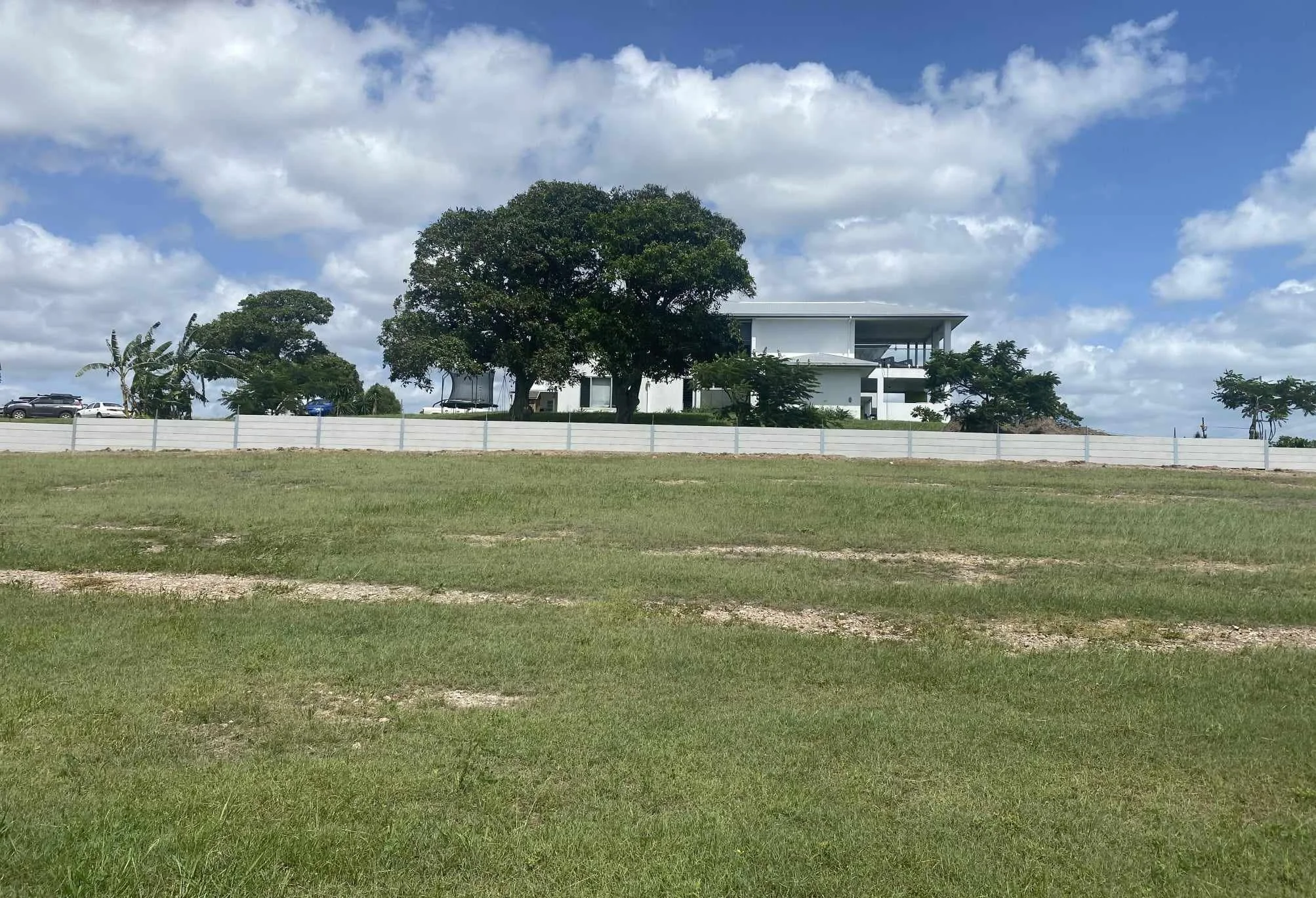A modern white house behind a grassy field with trees and a fence.