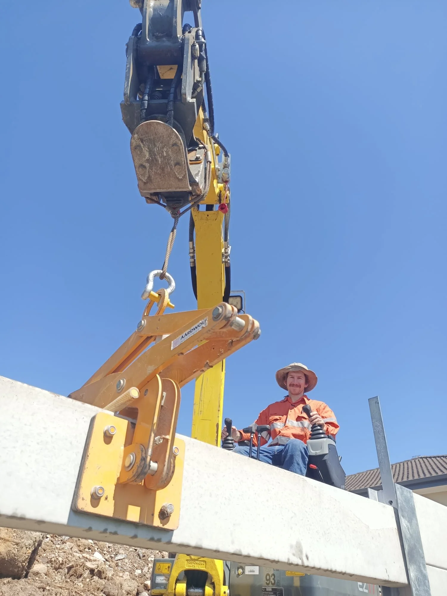 Construction worker sitting in a yellow excavator cab, maneuvering machinery to lift a concrete slab on a sunny day.