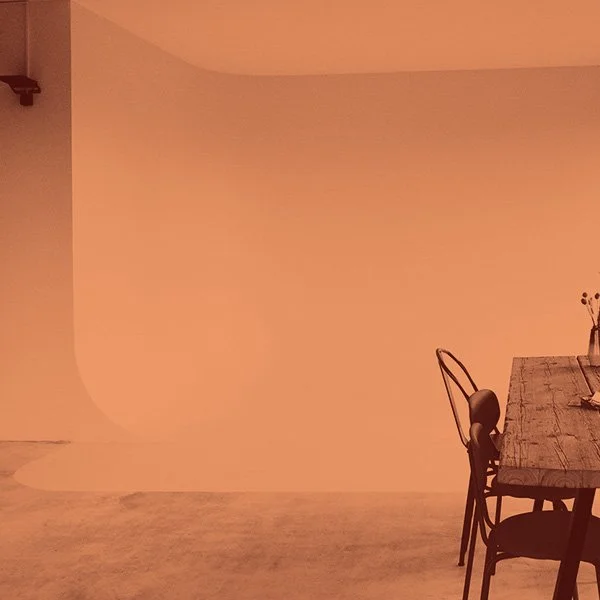 Ein minimalistischer Raum mit einem Holztisch und einem Stuhl. Der Hintergrund ist einfarbig und es sind wenige dekorative Elemente sichtbar.