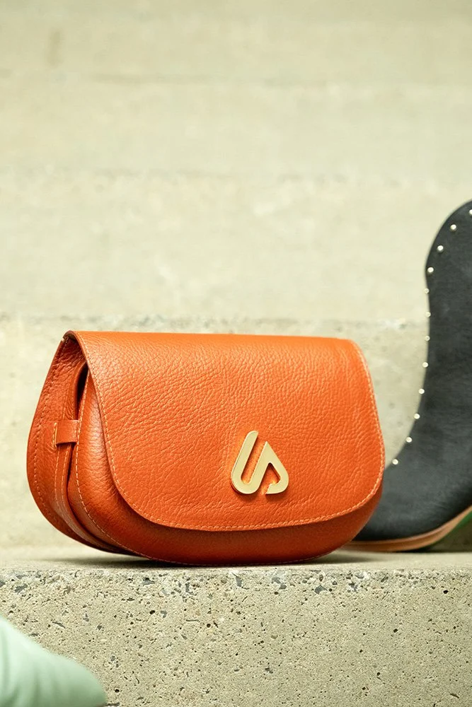 Orange Ledertasche mit Logo auf Betonstufen.