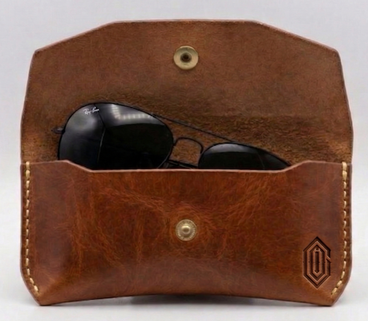 A brown leather sunglasses case with sunglasses inside, and a logo embossed on the lower right corner.