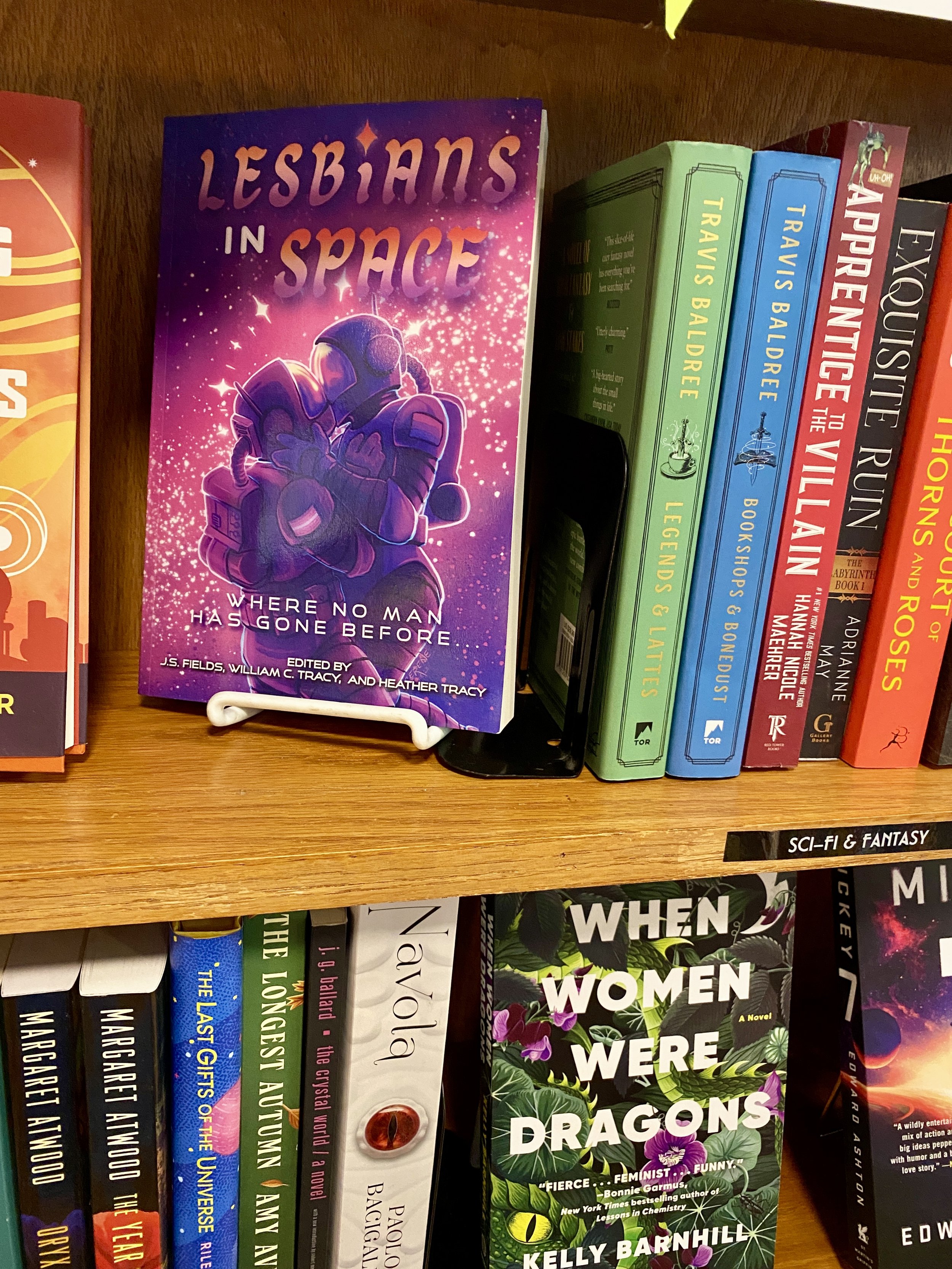 A photograph of a paperback edition of Lesbians in Space: Where No Man Has Gone Before, published by Space Wizard Science Fantasy, resting on a Sci-Fi and Fantasy display in a bookstore.