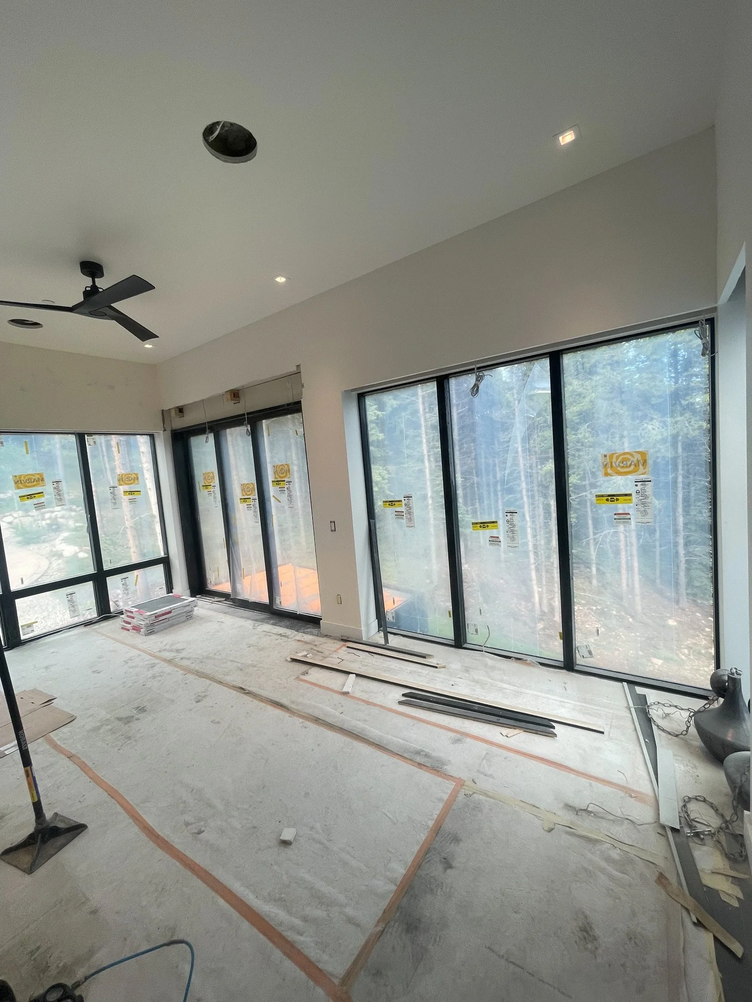 A room under construction with large glass windows, some construction materials, and tools on the floor.