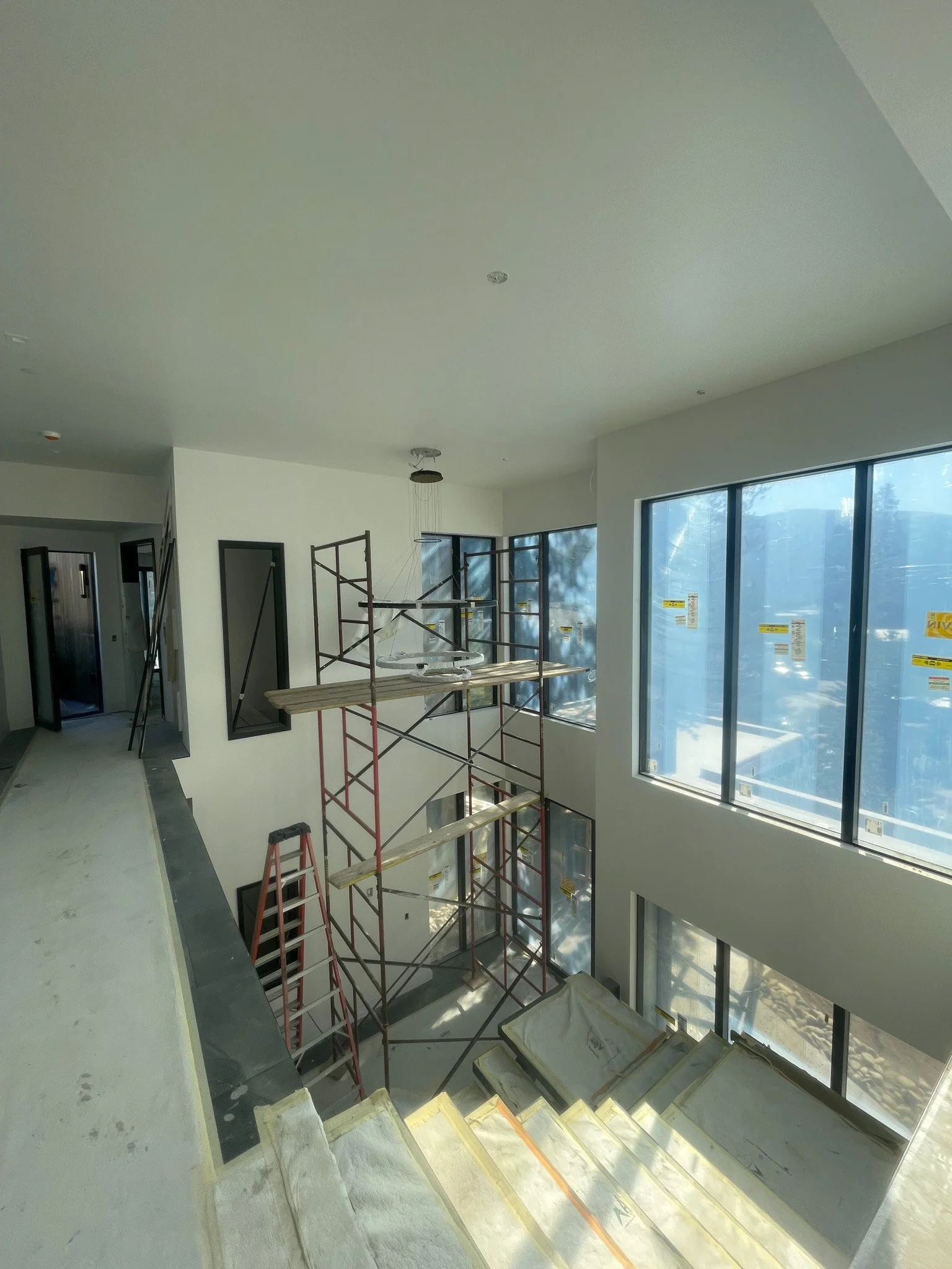 Interior of a building under construction with scaffolding, ladders, staircase, large window, and ongoing work.