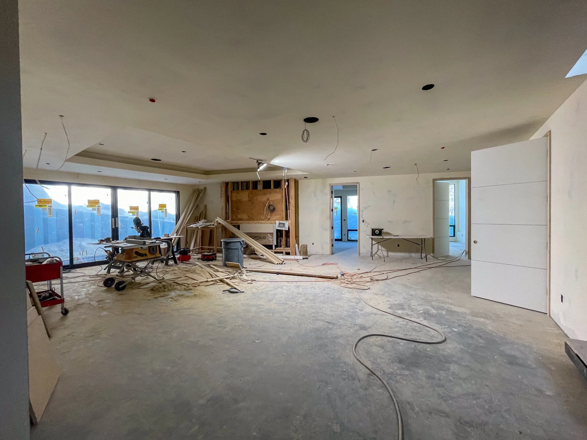 Interior of a house under construction, with unfinished walls, wiring, and construction tools scattered across the floor.