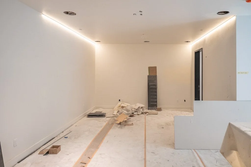 Empty room under construction with white walls, some construction materials on the floor, and a doorway on the right.