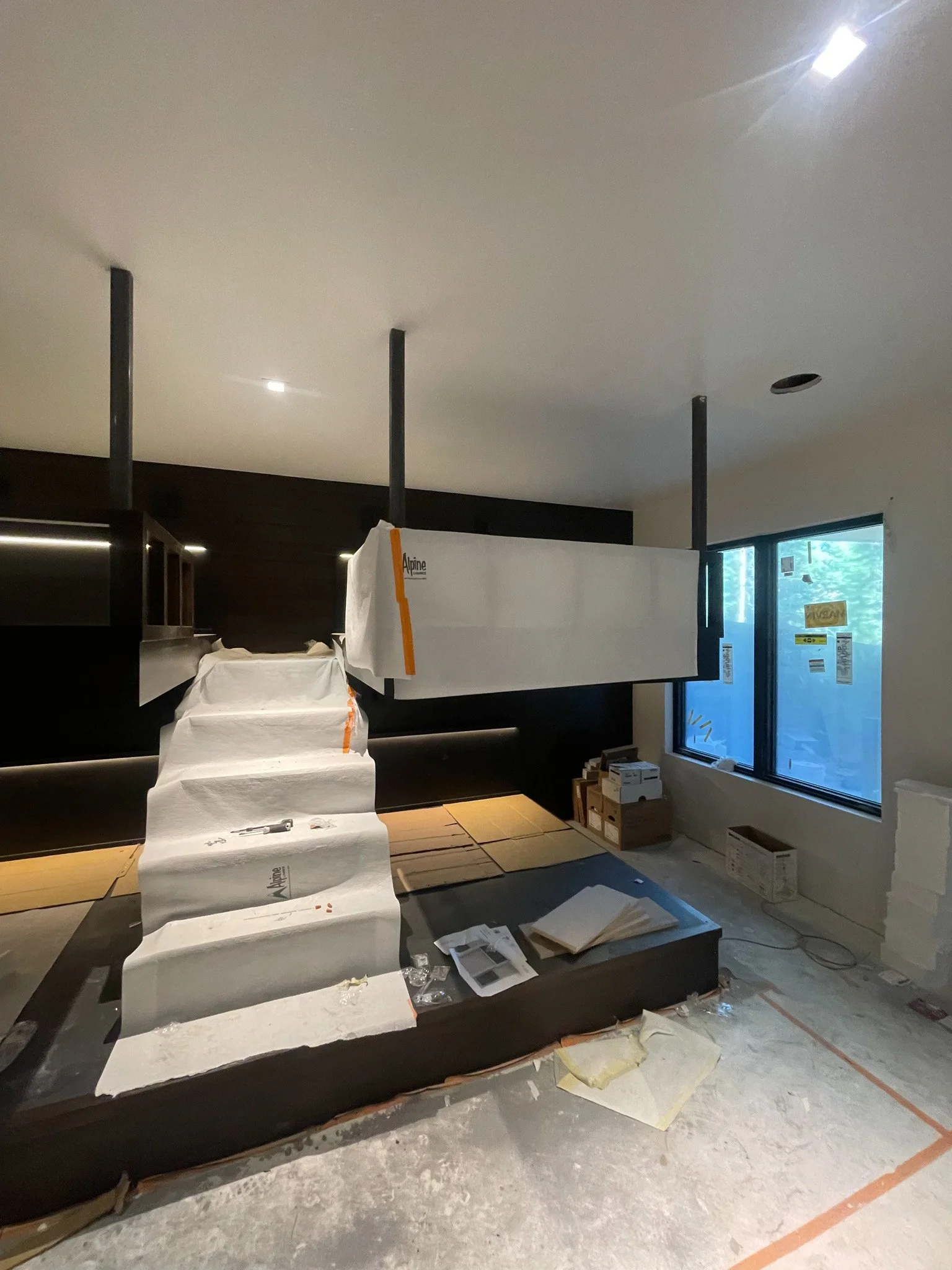 Interior of a room under construction with a suspended structure, steps, and construction materials scattered on the floor.