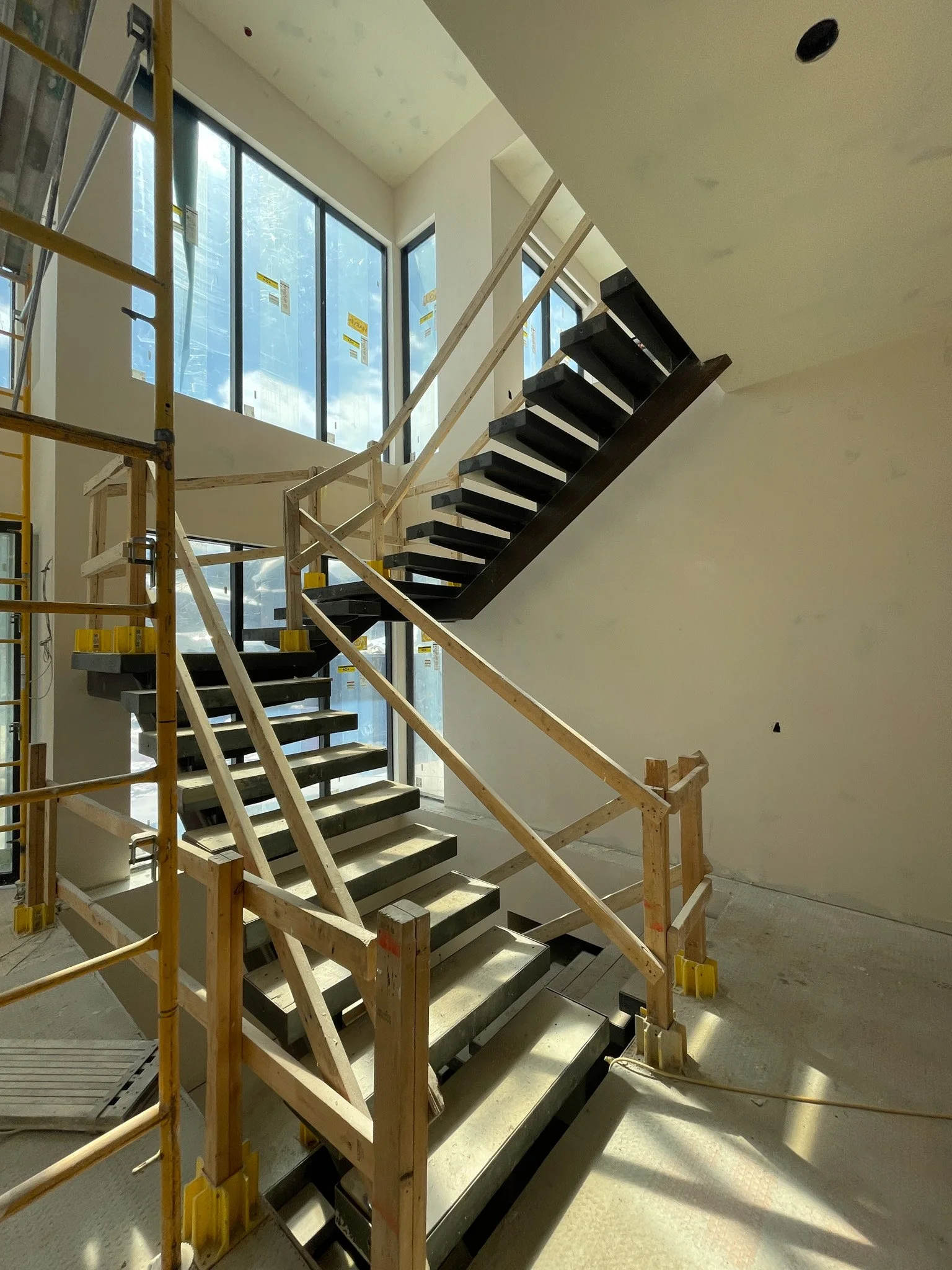 Indoor construction site with a partially built staircase, wooden scaffolding, and large windows.