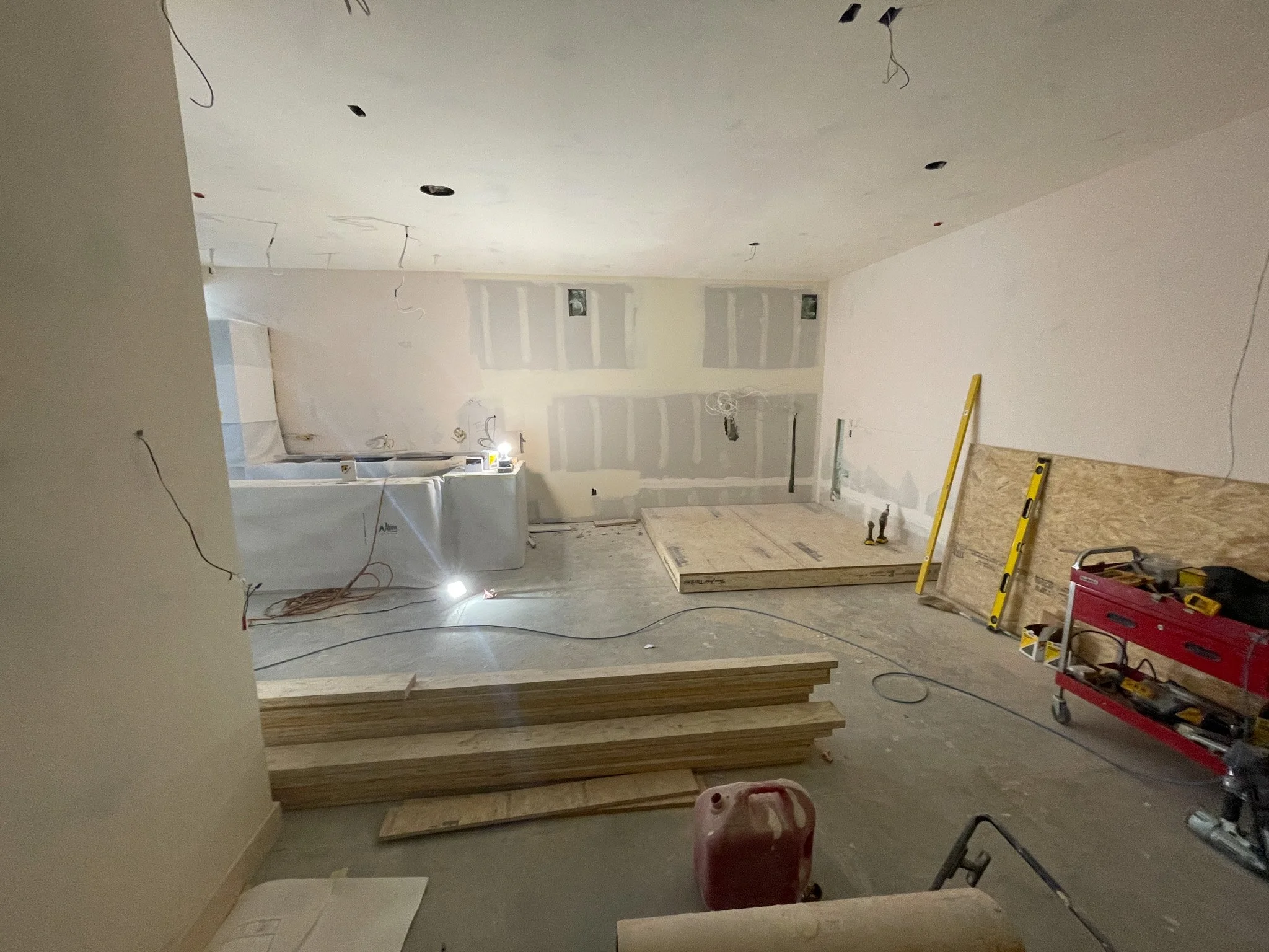 An unfinished room under construction with drywall and ceiling work in progress, construction tools, wooden planks, and building materials scattered around.