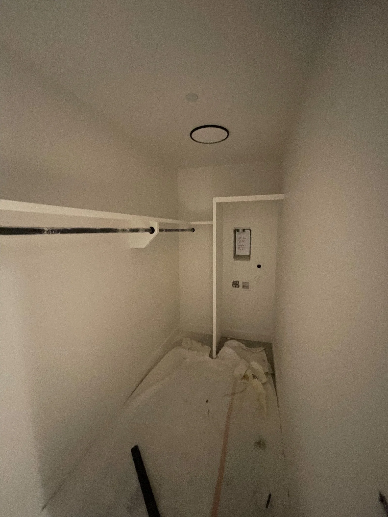 Empty closet with a hanging rod, a divider, and a wall with electrical panels, cluttered with packing materials and debris.