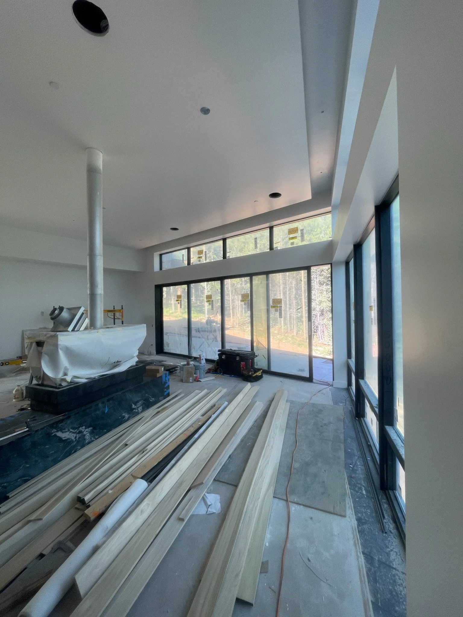 Interior view of a modern building under construction with large glass windows, construction tools, and materials scattered on the floor.